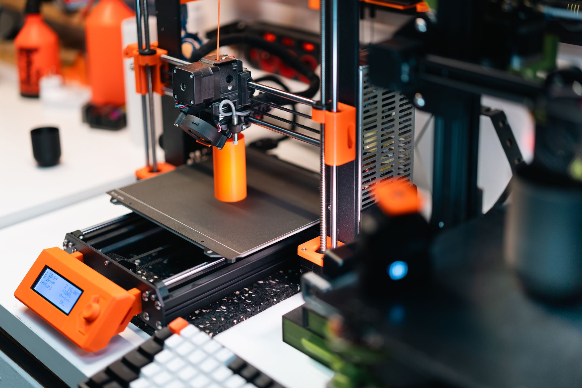 3D printer operating in a workshop, creating a prototype with orange accents.