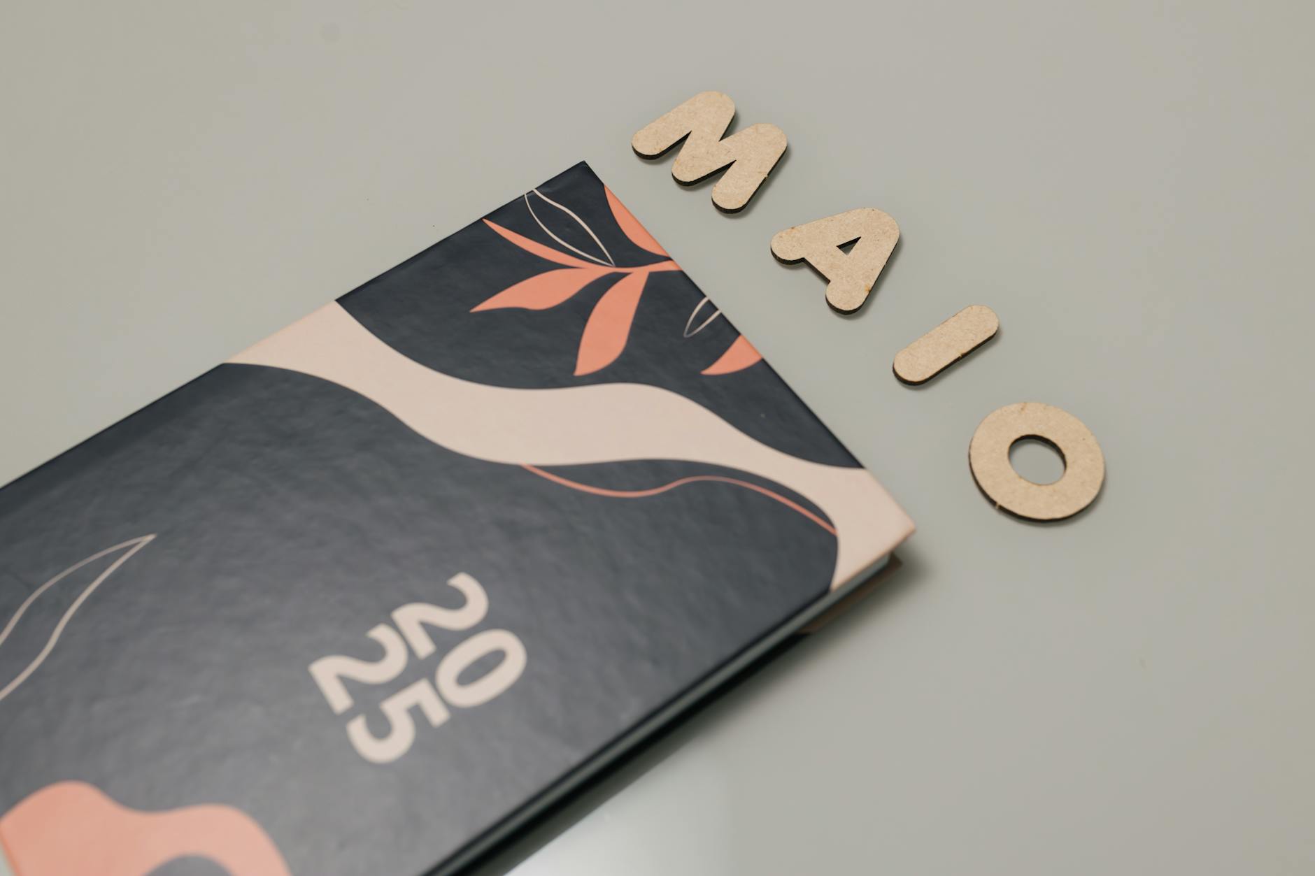 A stylish 2025 planner with modern abstract design next to wooden letters spelling 'MAIO'.