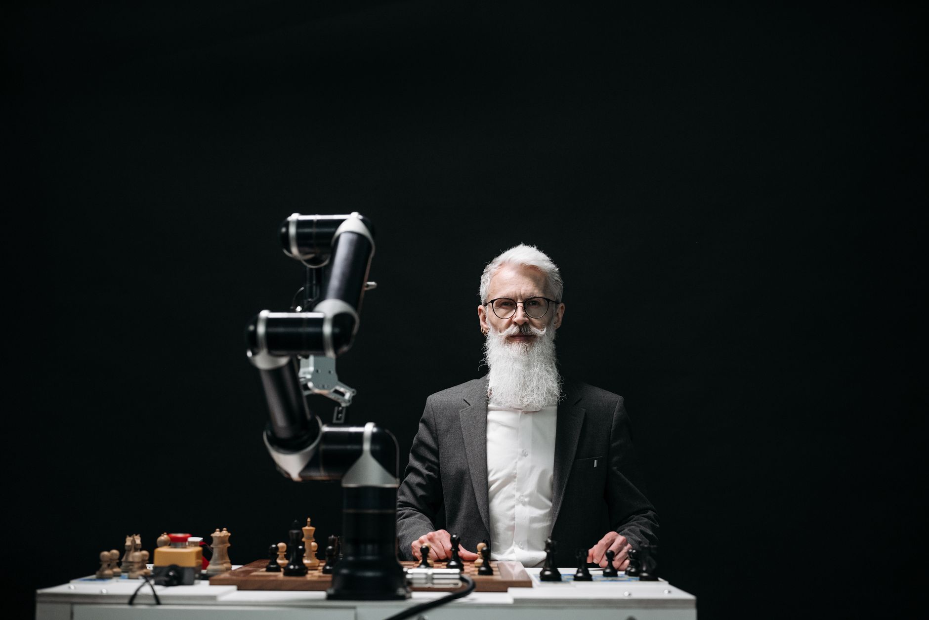 A bearded man in suit playing chess with robotic arm, showcasing AI strategy.