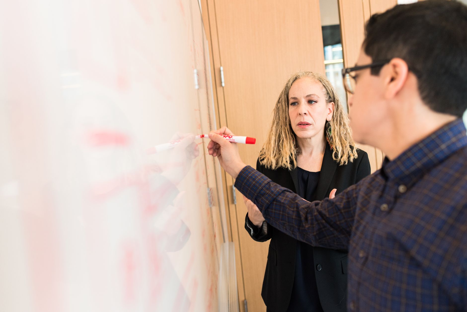 Two professionals collaborating during a business meeting, writing on a whiteboard.