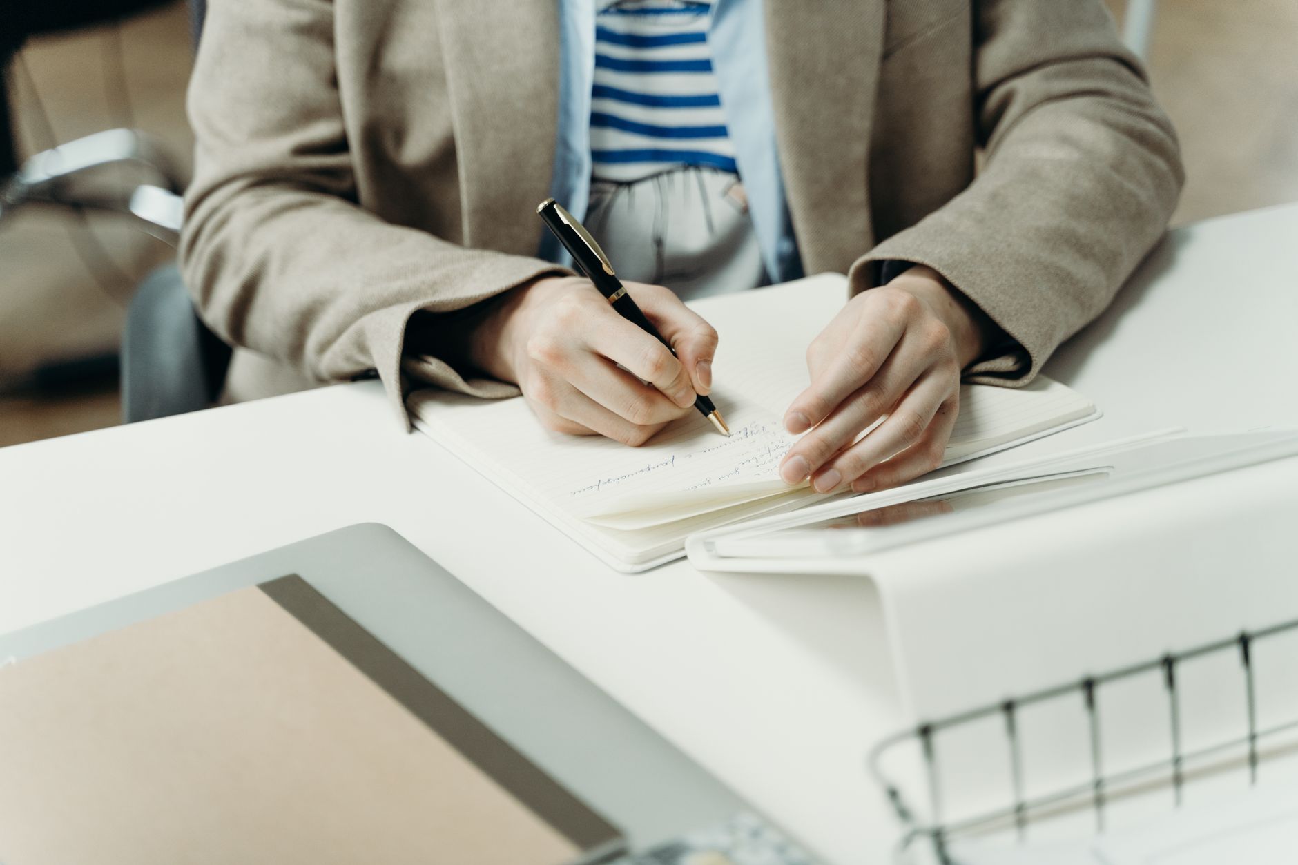 Close-up of an adult writing in a notebook at a modern office desk, capturing professional planning.