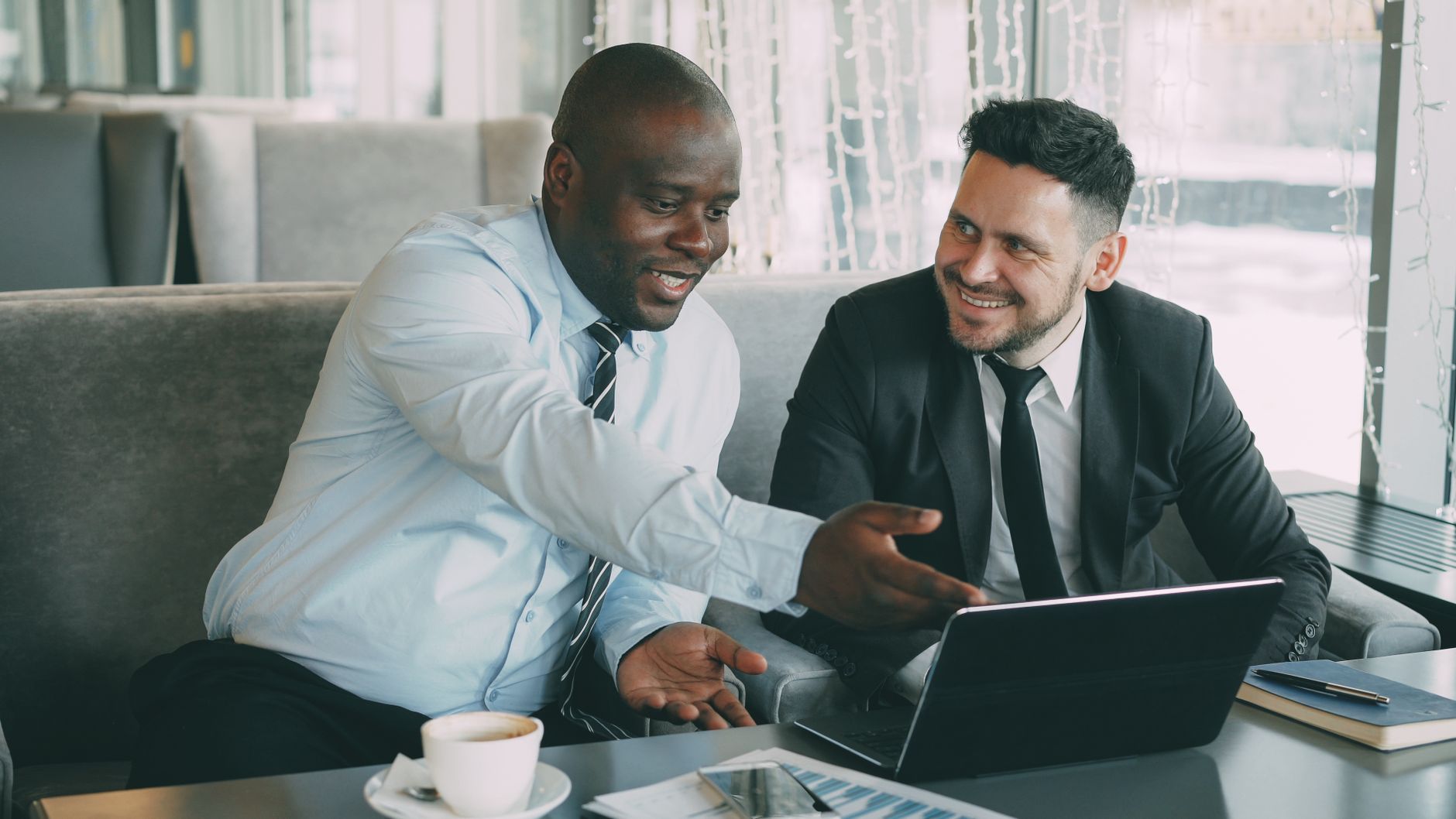 Two business professionals in a discussion over laptops in a modern cafe setting.
