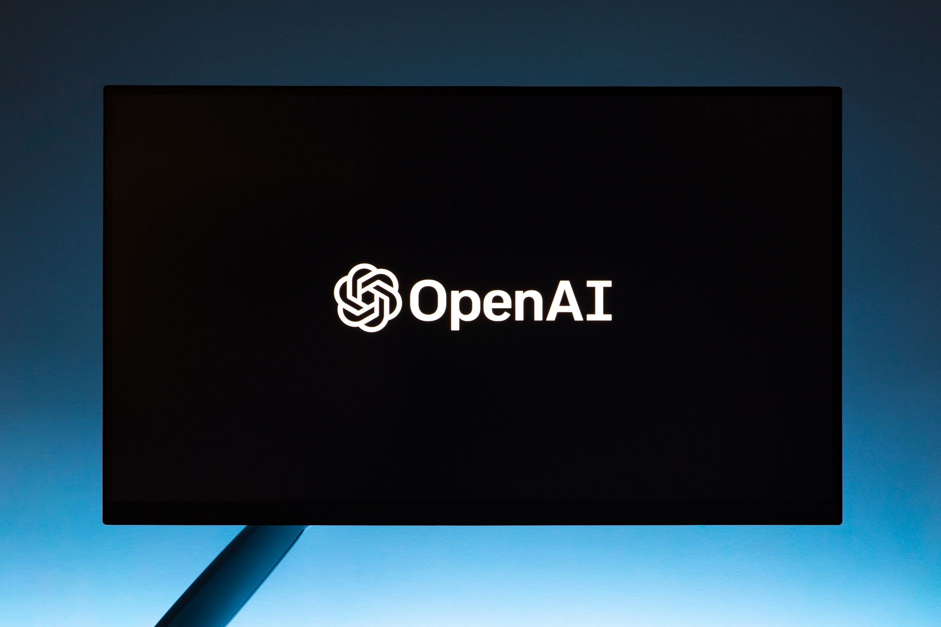 Minimalist display of OpenAI logo on a screen, set against a gradient blue background.