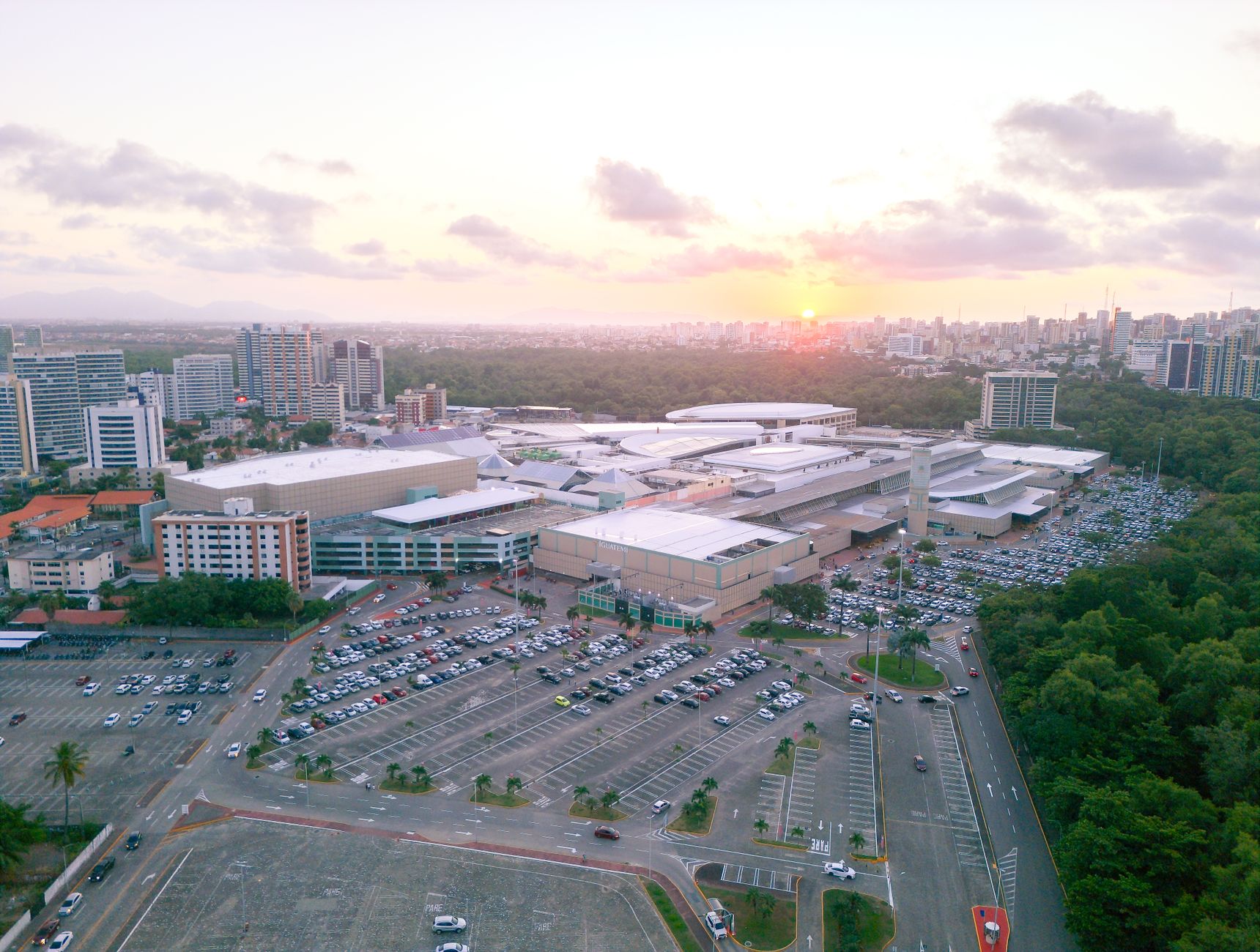 Bird's eye view of Fortaleza's urban landscape with lush forest and city buildings at sunset.