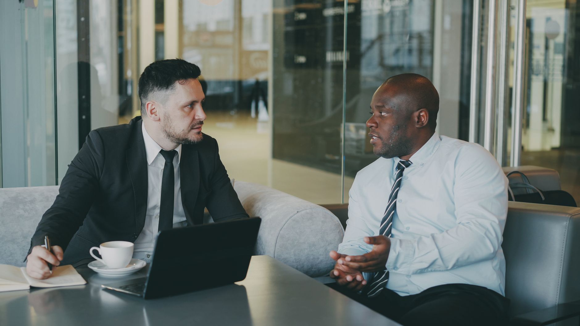 Two businessmen discussing at a cafe with a laptop and coffee.
