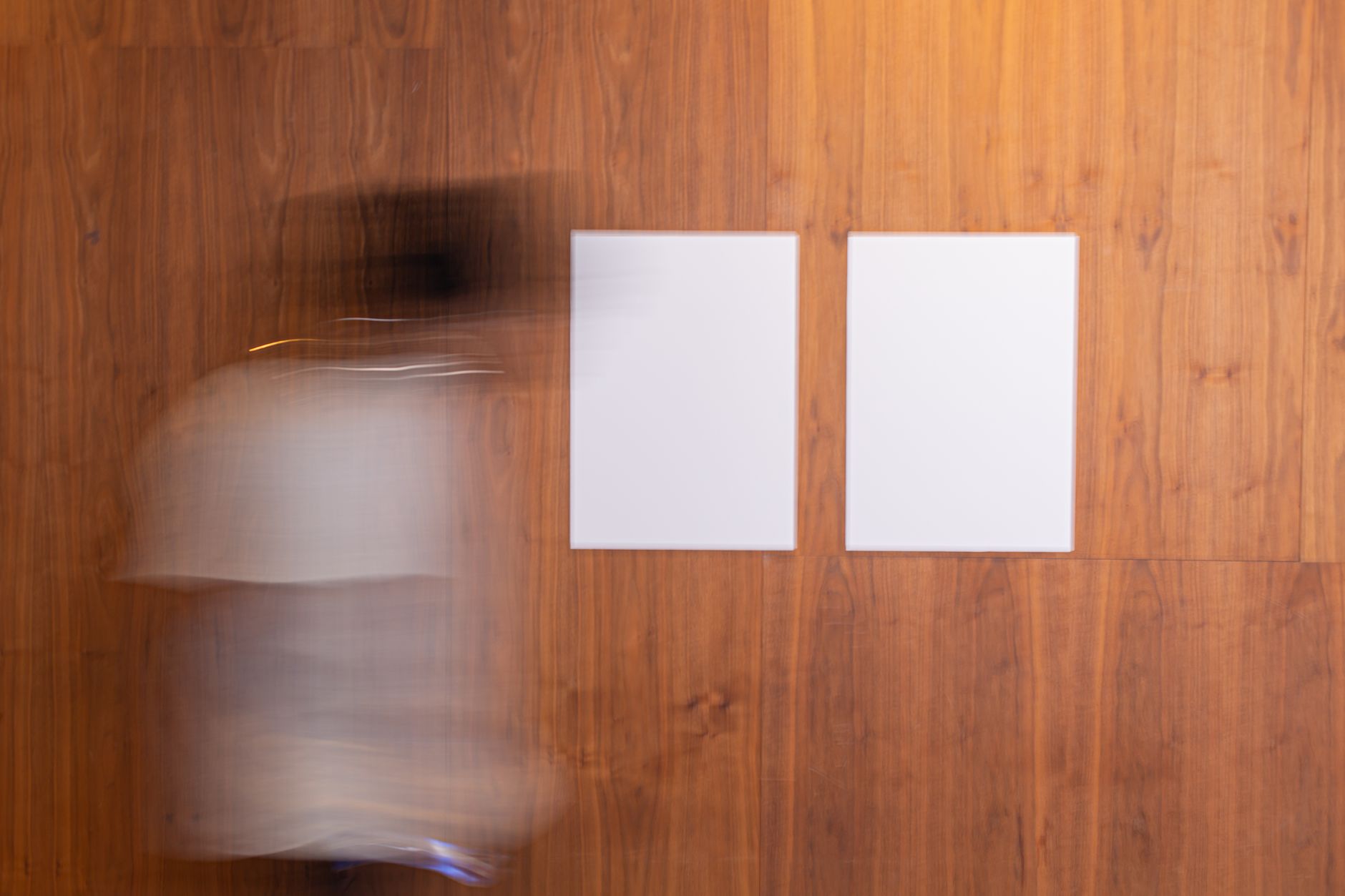 Side view of unrecognizable blurred person in motion strolling along wooden wall with white mock up placard in light room
