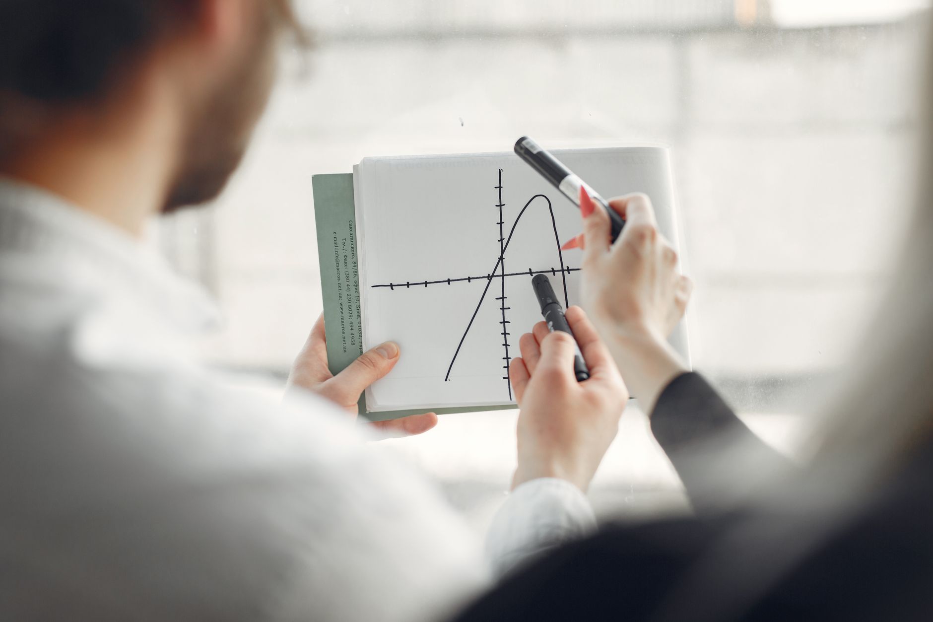 Two professionals discussing a parabola graph on a notebook, promoting teamwork and collaboration.