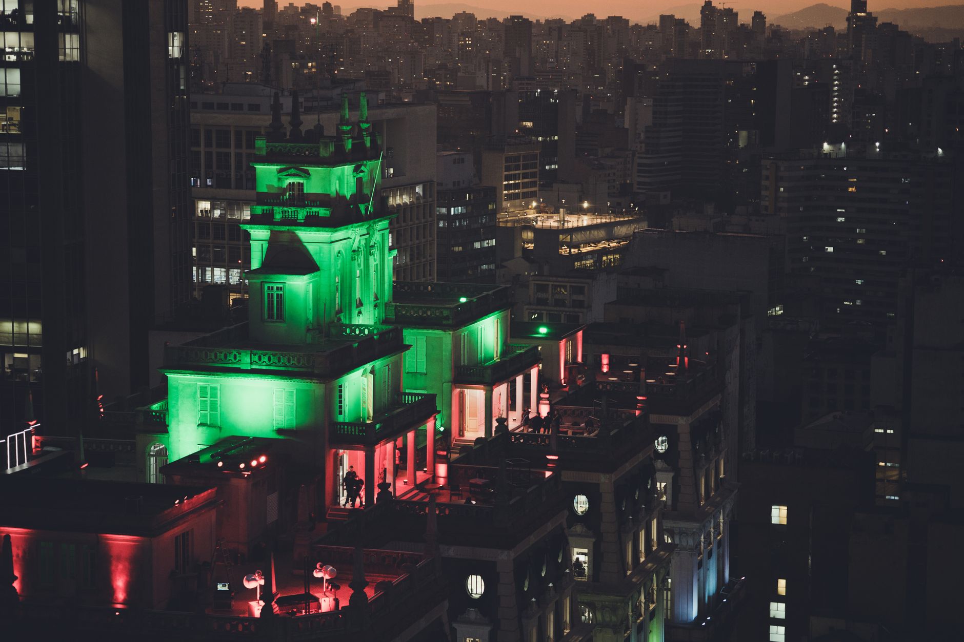 A vibrant view of São Paulo's skyline with a vividly lit rooftop and city lights at dusk.