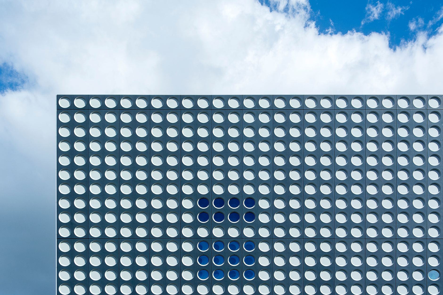 Abstract view of a modern building facade in Utrecht featuring circular patterns and a cloudy sky.