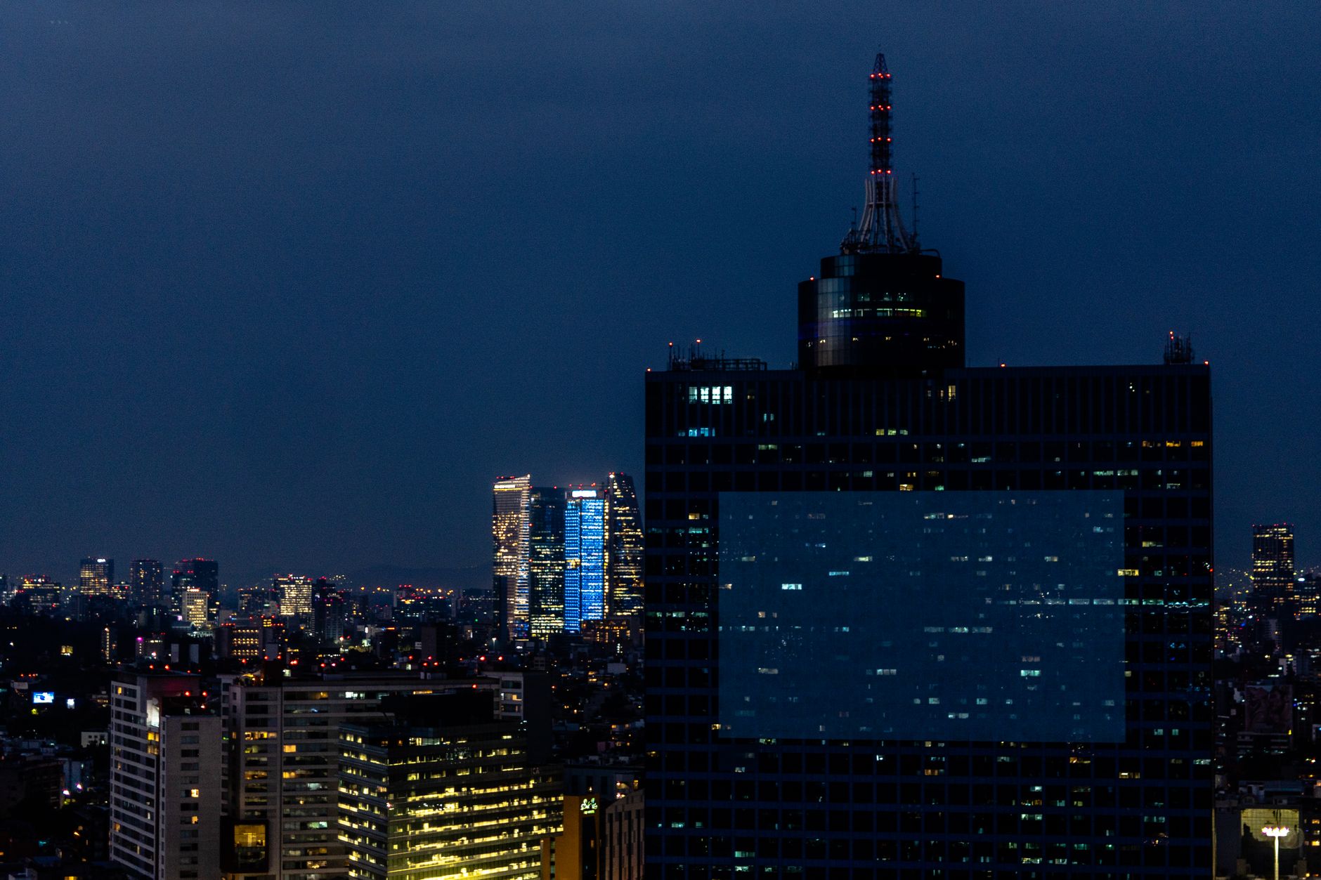 Evening cityscape of Ciudad de México with illuminated skyscrapers under a twilight sky.