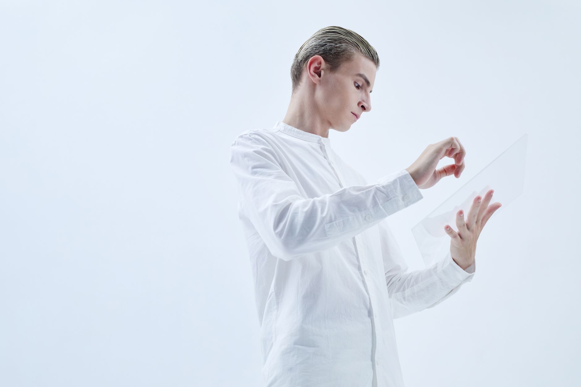 Young man interacting with a transparent digital tablet in a minimalist studio setting.