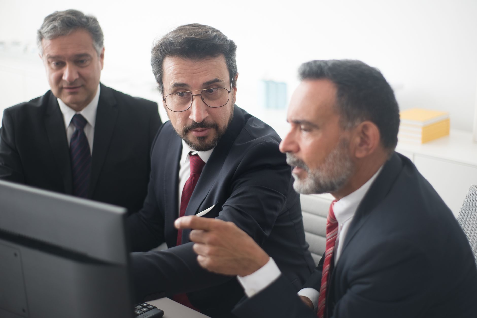 Three men in a corporate meeting discussing a project in a modern office.