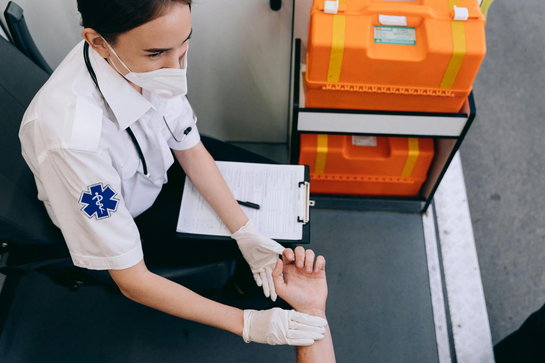 A paramedic in a mask checks a patient's pulse inside an ambulance for medical assessment.