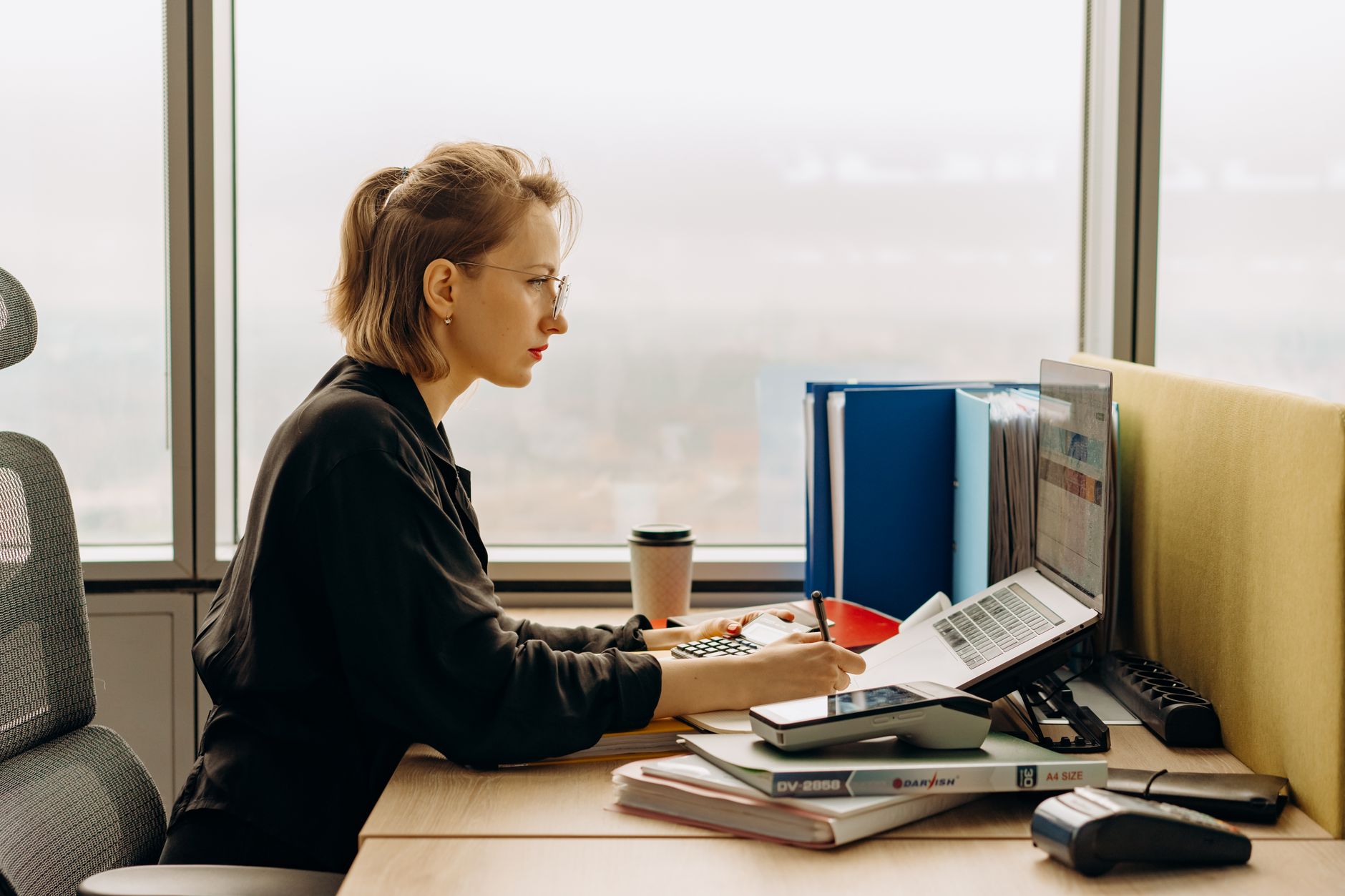 Dedicated woman using laptop and calculator in modern office setting.