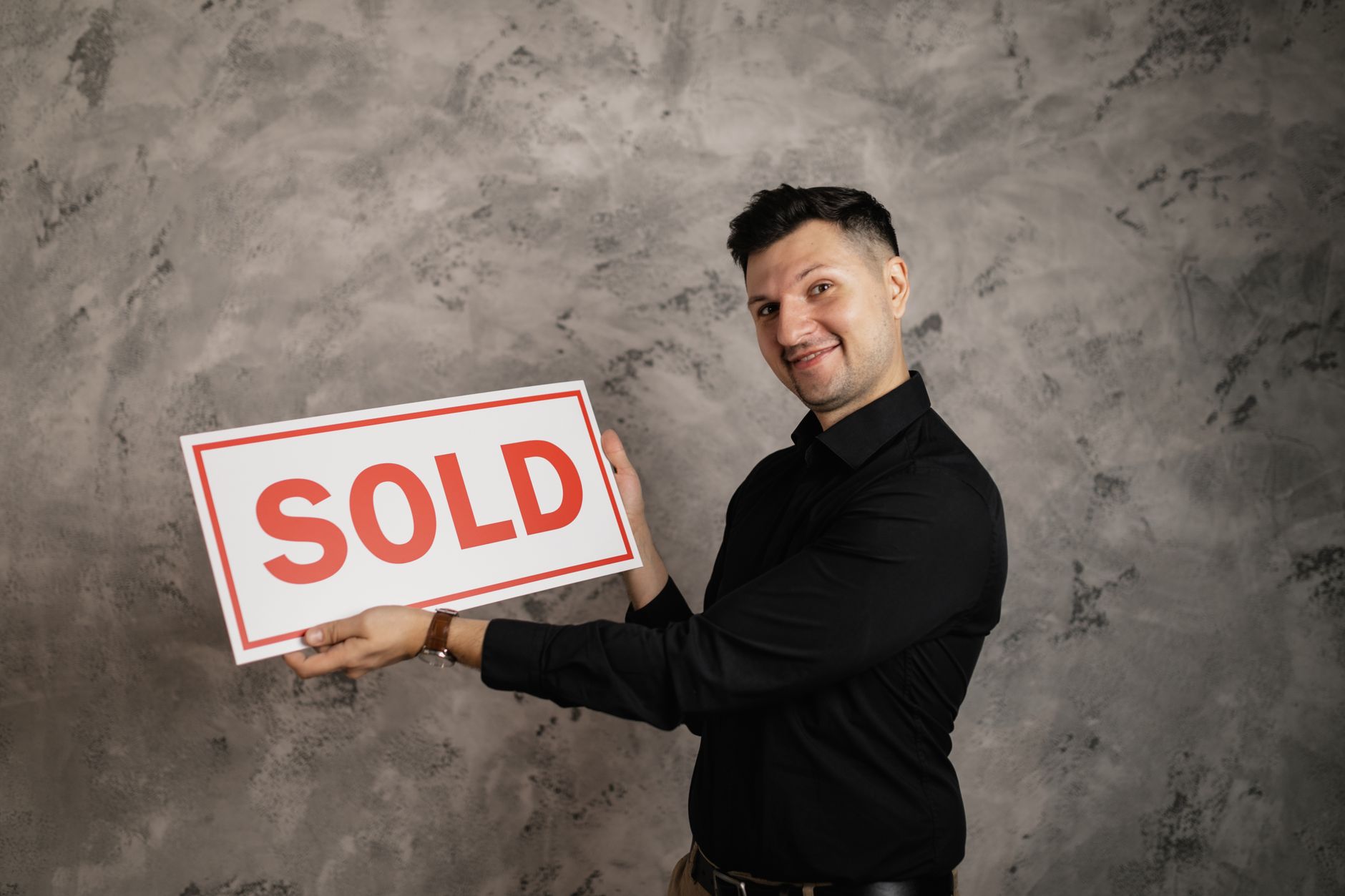Happy realtor holding a 'Sold' sign, symbolizing successful property sale.