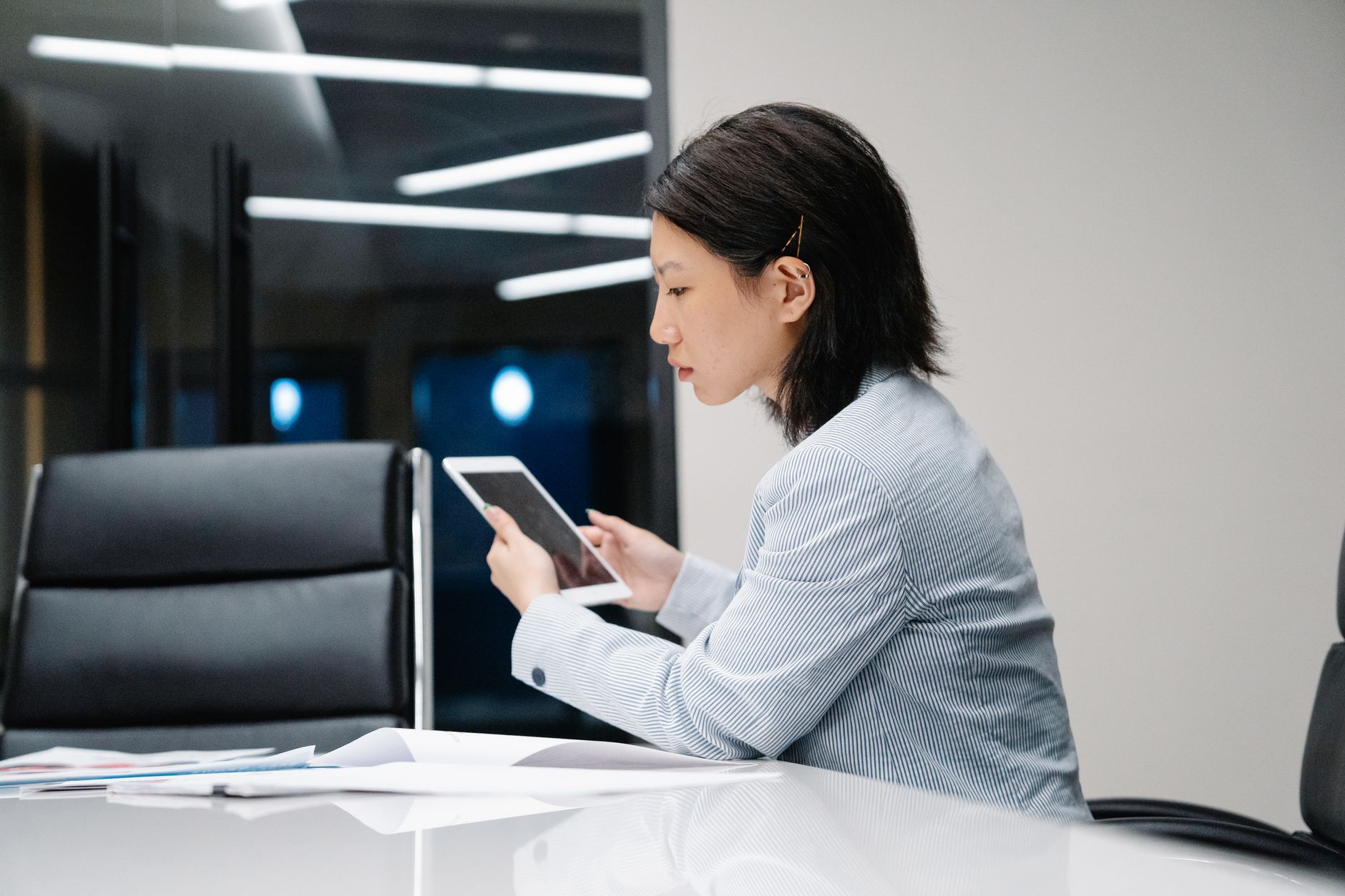 Asian woman absorbed in work on a tablet in a sleek office setting.