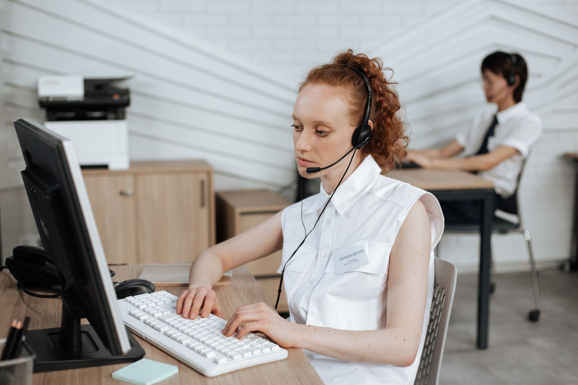 Focused call center agent working on her computer with headset in a modern office setting.