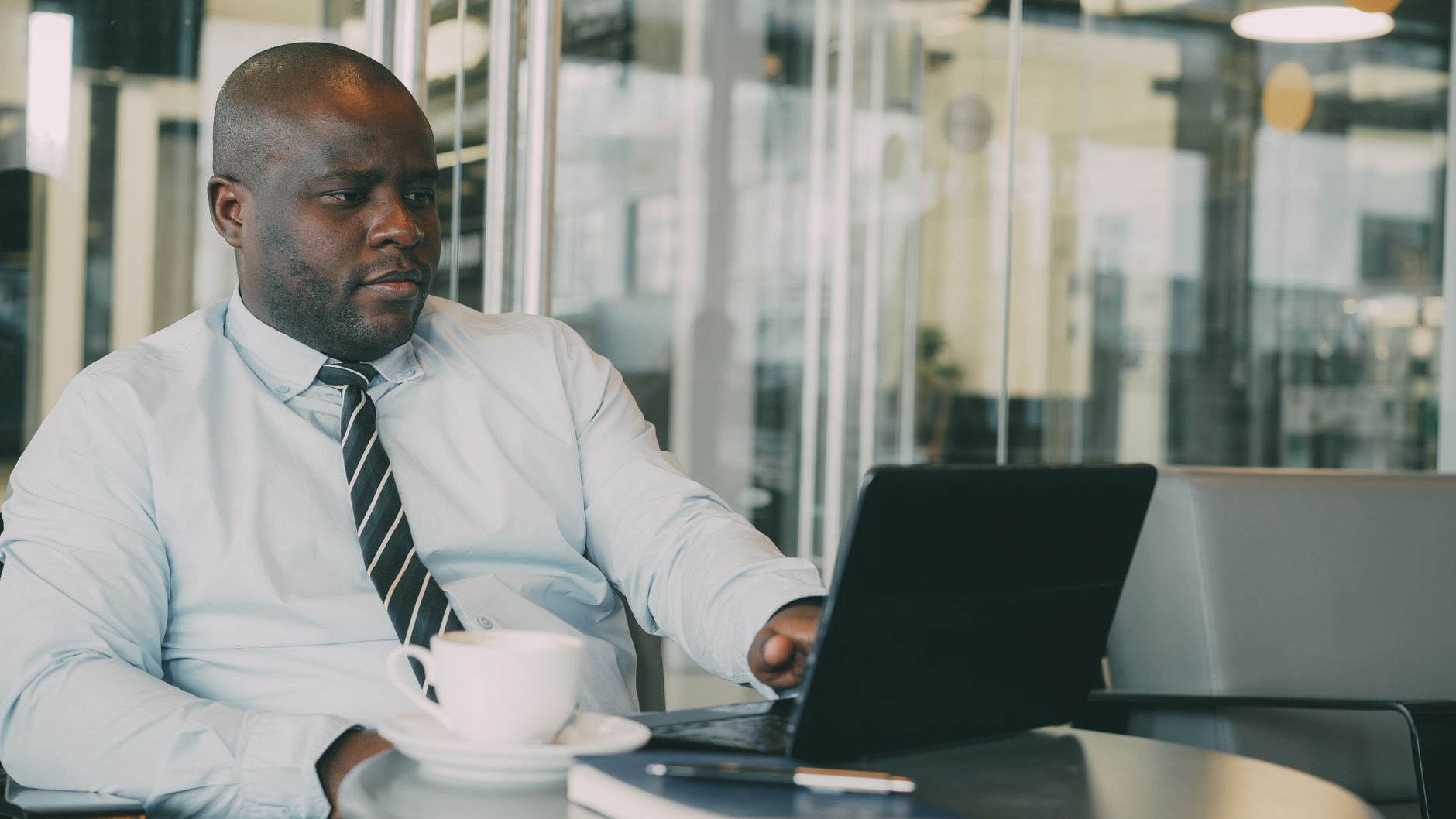 Focused businessman uses laptop in stylish cafe, sipping coffee. Perfect for business or lifestyle themes.
