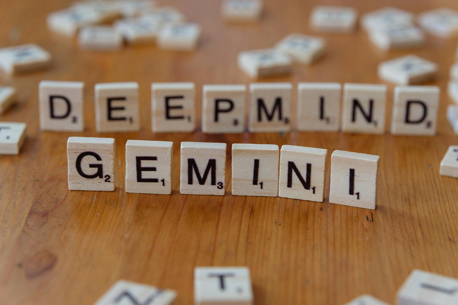 Wooden Scrabble tiles spelling 'Deepmind' and 'Gemini' on a wooden surface, a concept of AI and games.