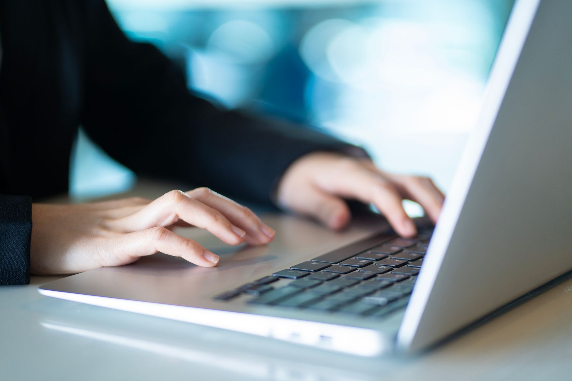 Close-up of hands typing on a laptop in a bright, modern office, symbolizing productivity and digital work.