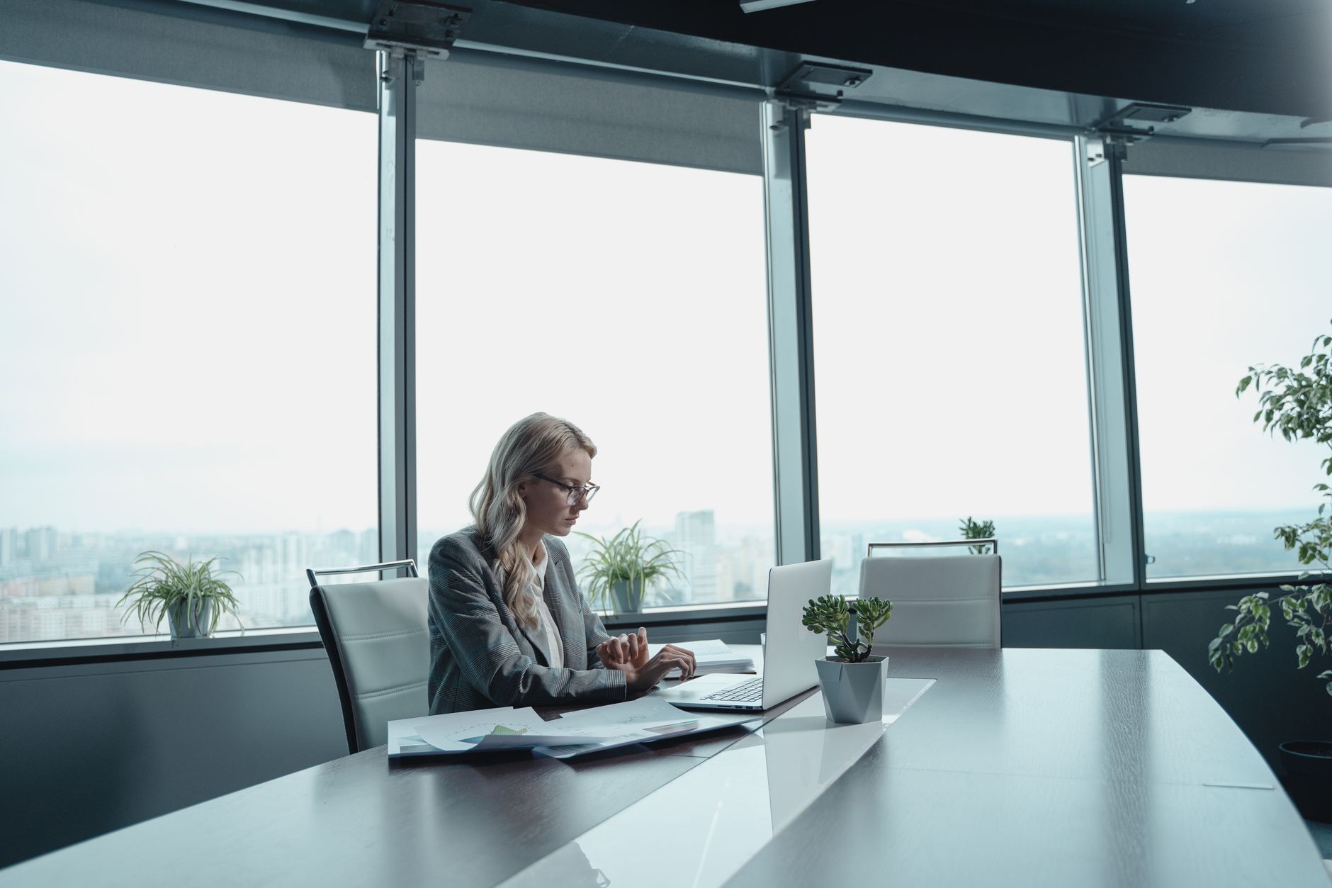 Woman with laptop working in a bright, modern office with large windows.
