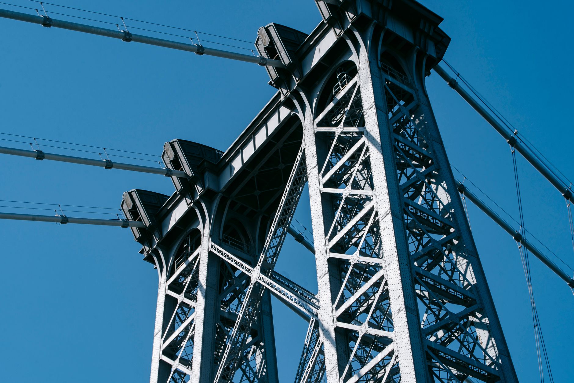 From below of suspension Williamsburg Bridge with long metal constructions against cloudless sky