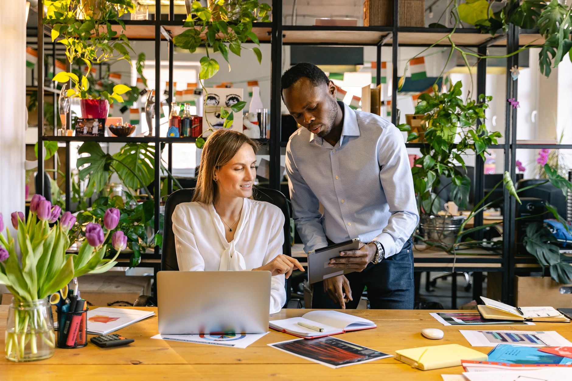 Two professionals engaging in a collaborative discussion in a foliage-filled office.