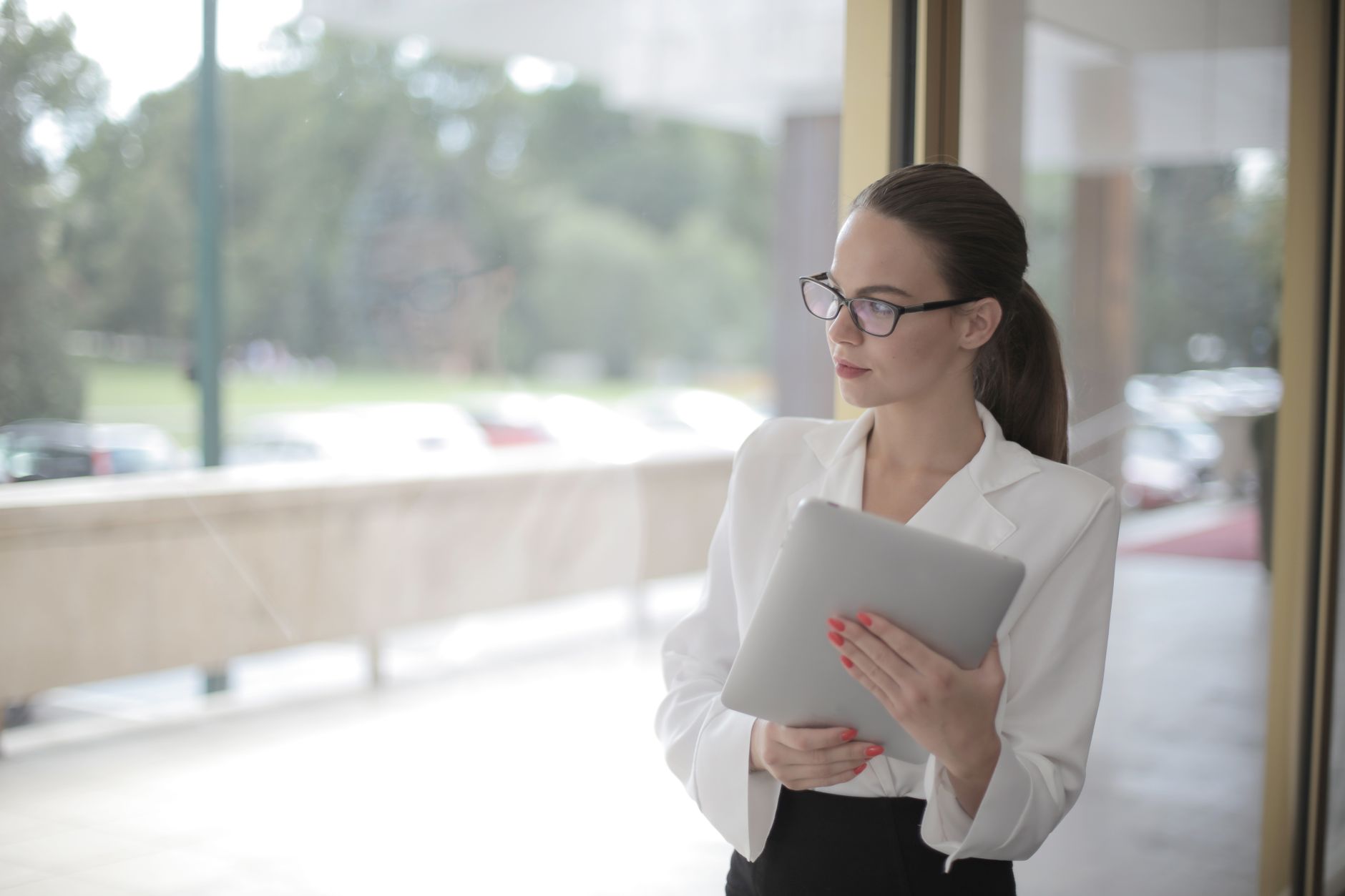 Businesswoman in office holding a tablet, looking thoughtfully out the window.