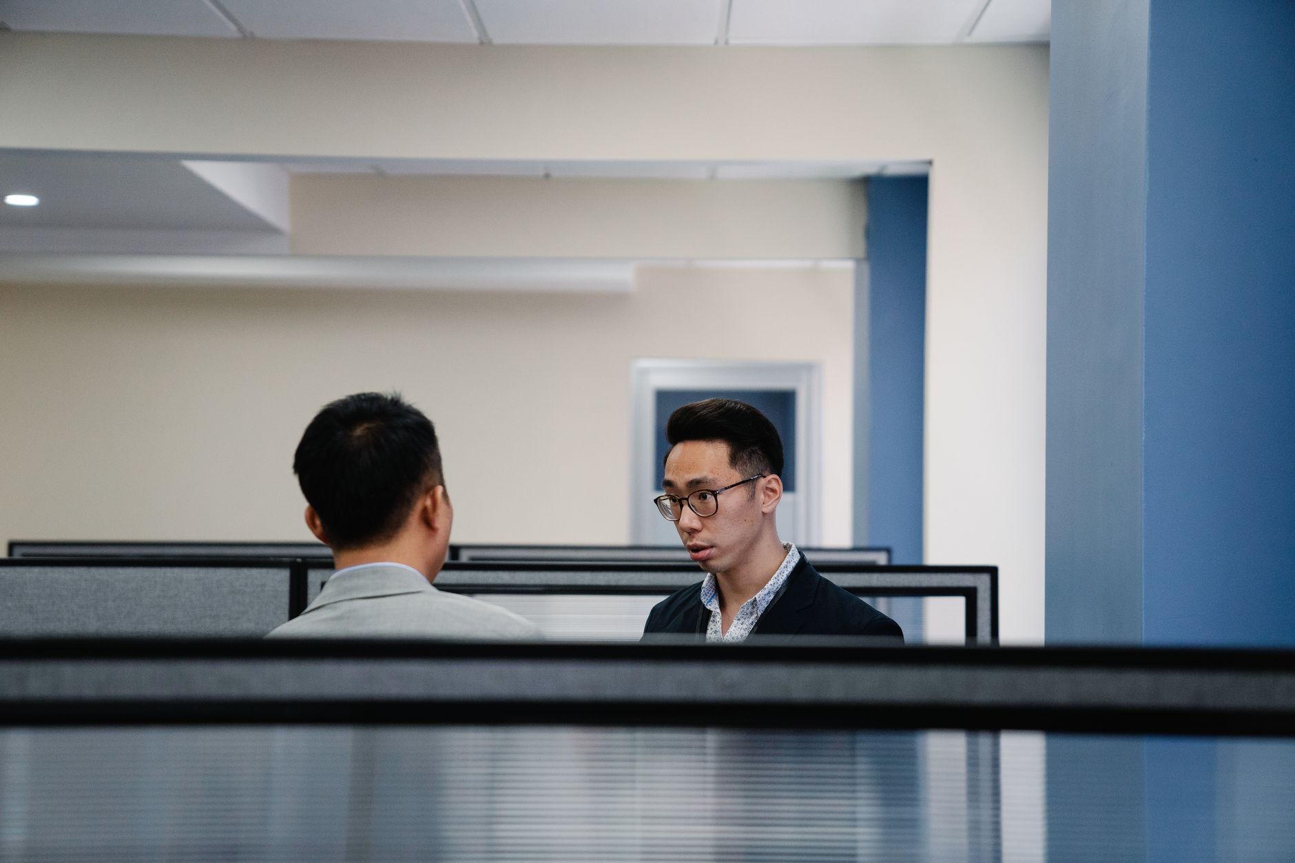 Two professionals engaged in conversation within an office cubicle setting.