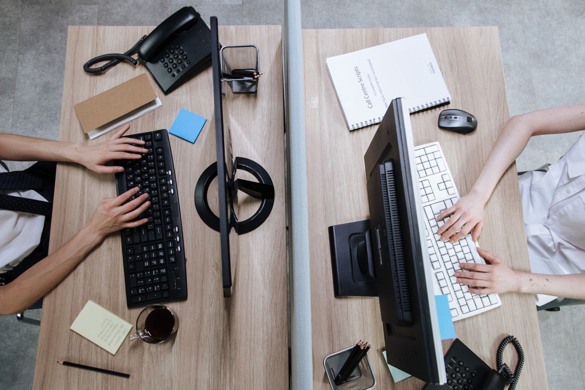 Top view of two workstations with people typing on keyboards, during the day in an office setting.