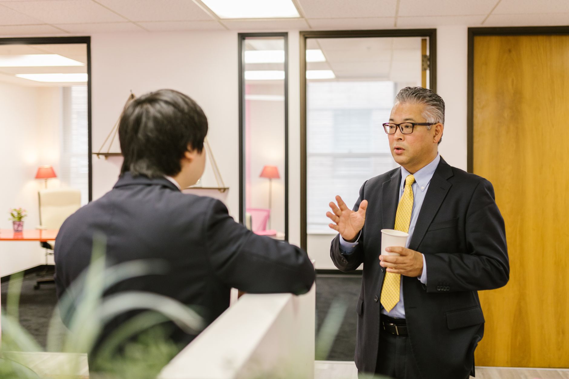 Two businessmen in formal attire having a conversation in an office setting.