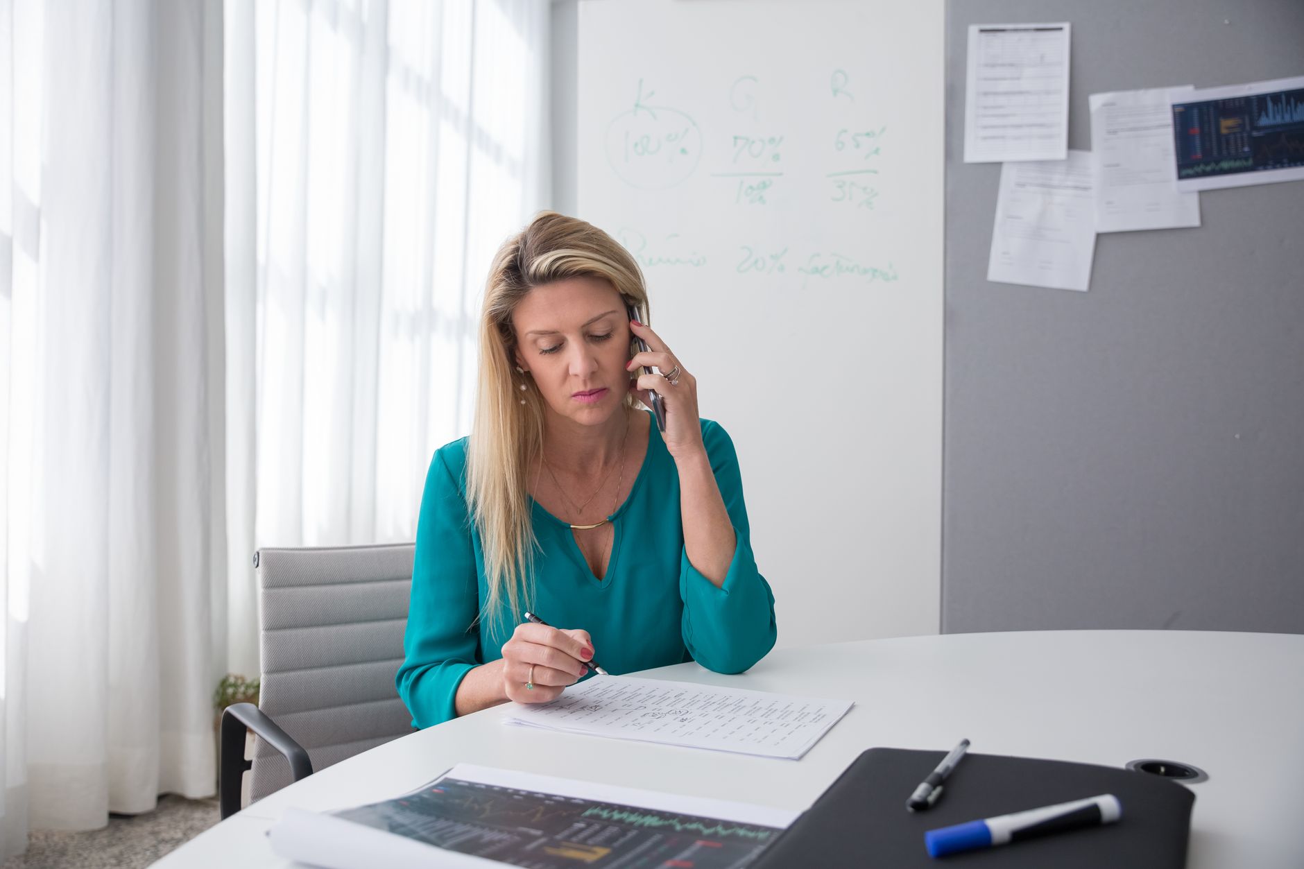 Professional woman in an office multitasking on the phone while writing notes, exuding focus and productivity.