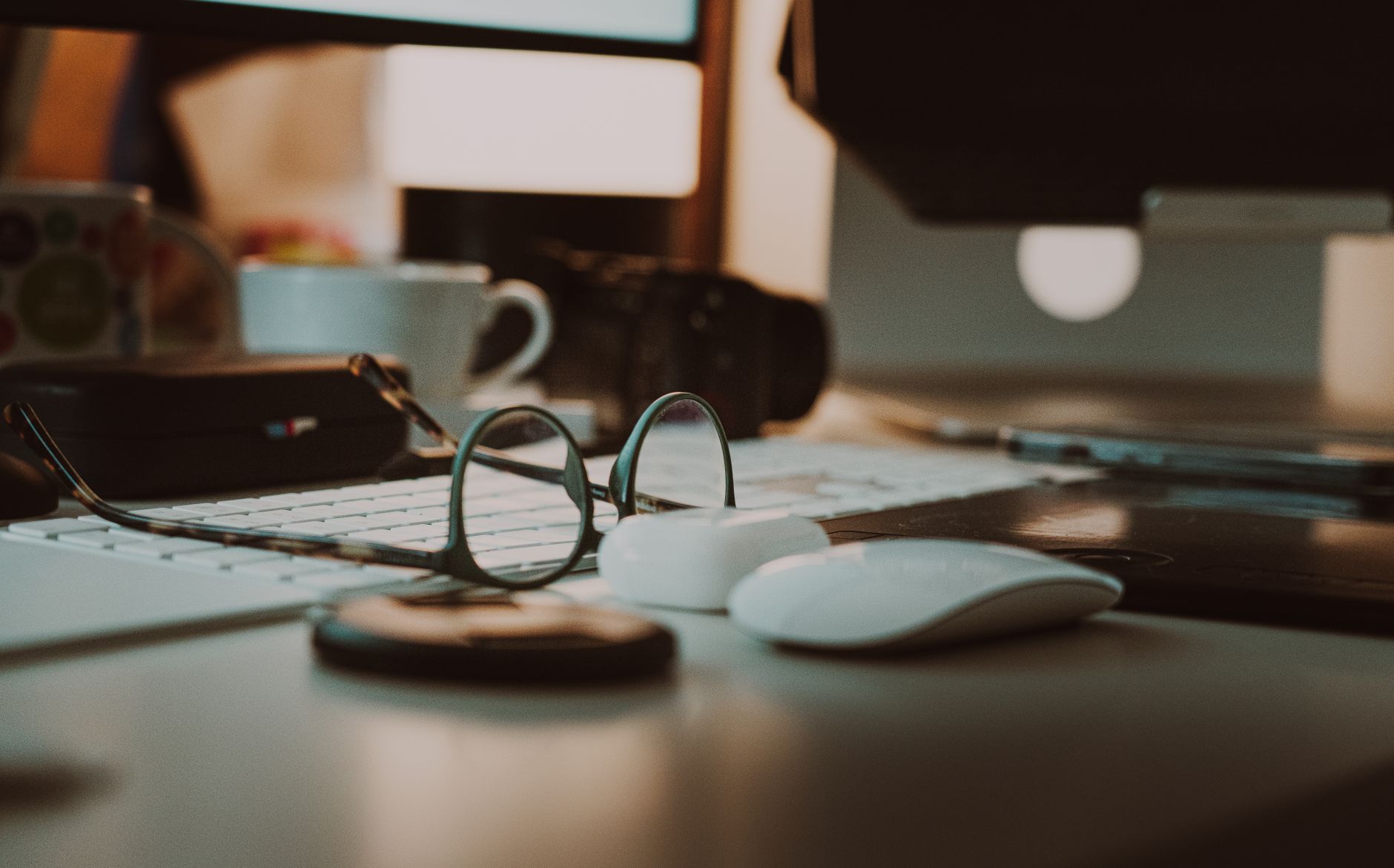 A modern home office setup featuring glasses, keyboard, and coffee on a desk.