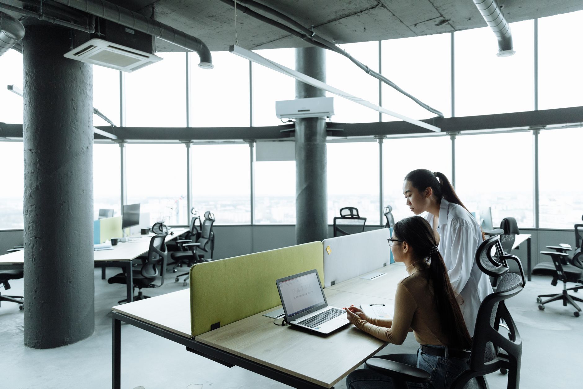 Two Asian women collaborating in a modern office environment focused on teamwork and innovation.