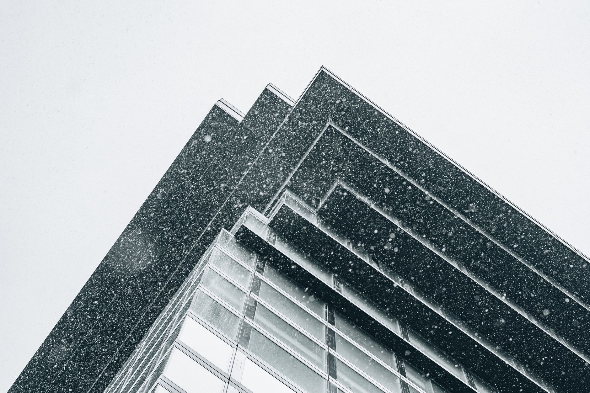 Low angle shot of a modern building's facade during a snowy winter day, showcasing architectural lines.