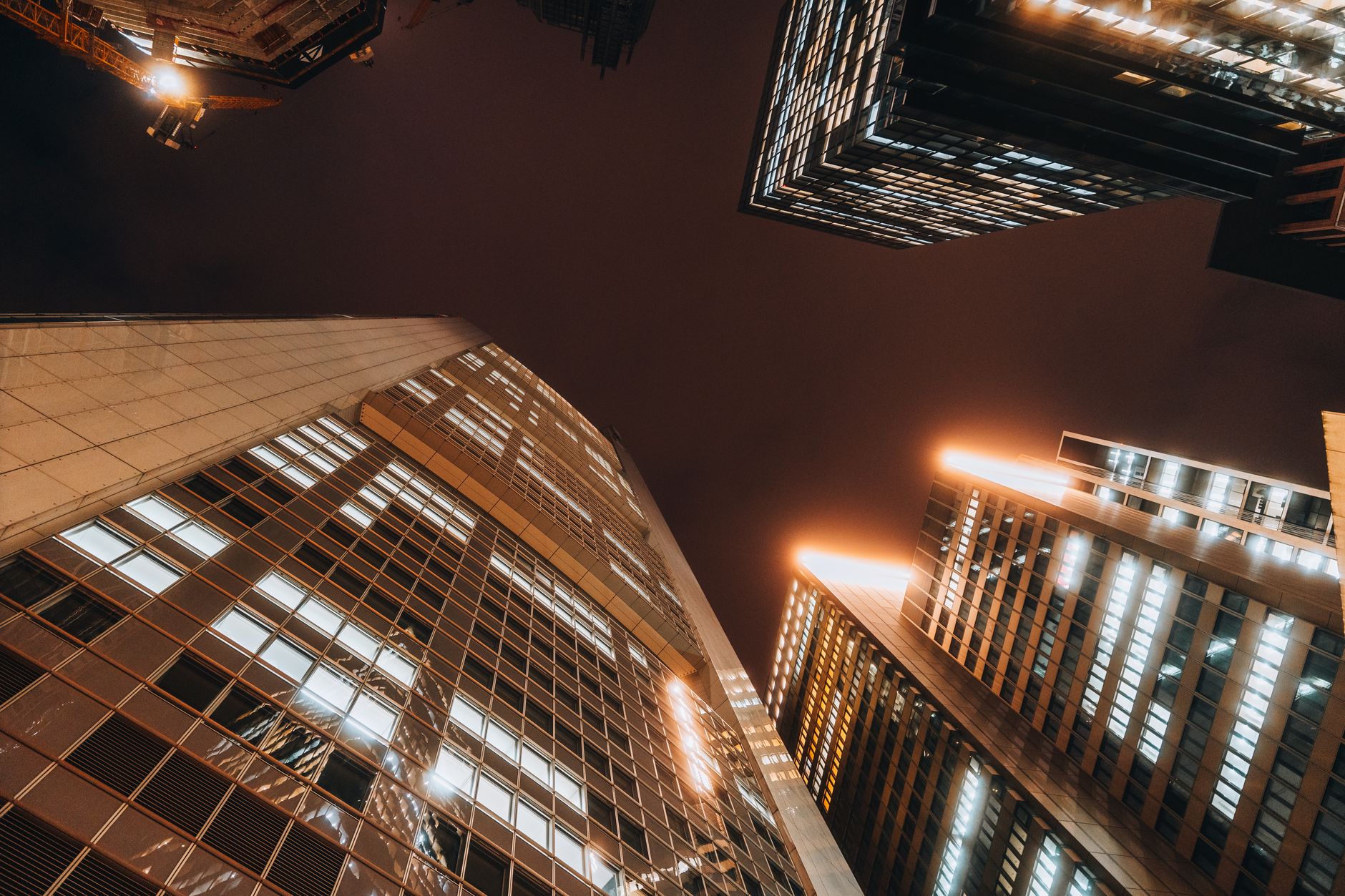 A dramatic view of illuminated skyscrapers reaching into the night sky in a bustling urban downtown.