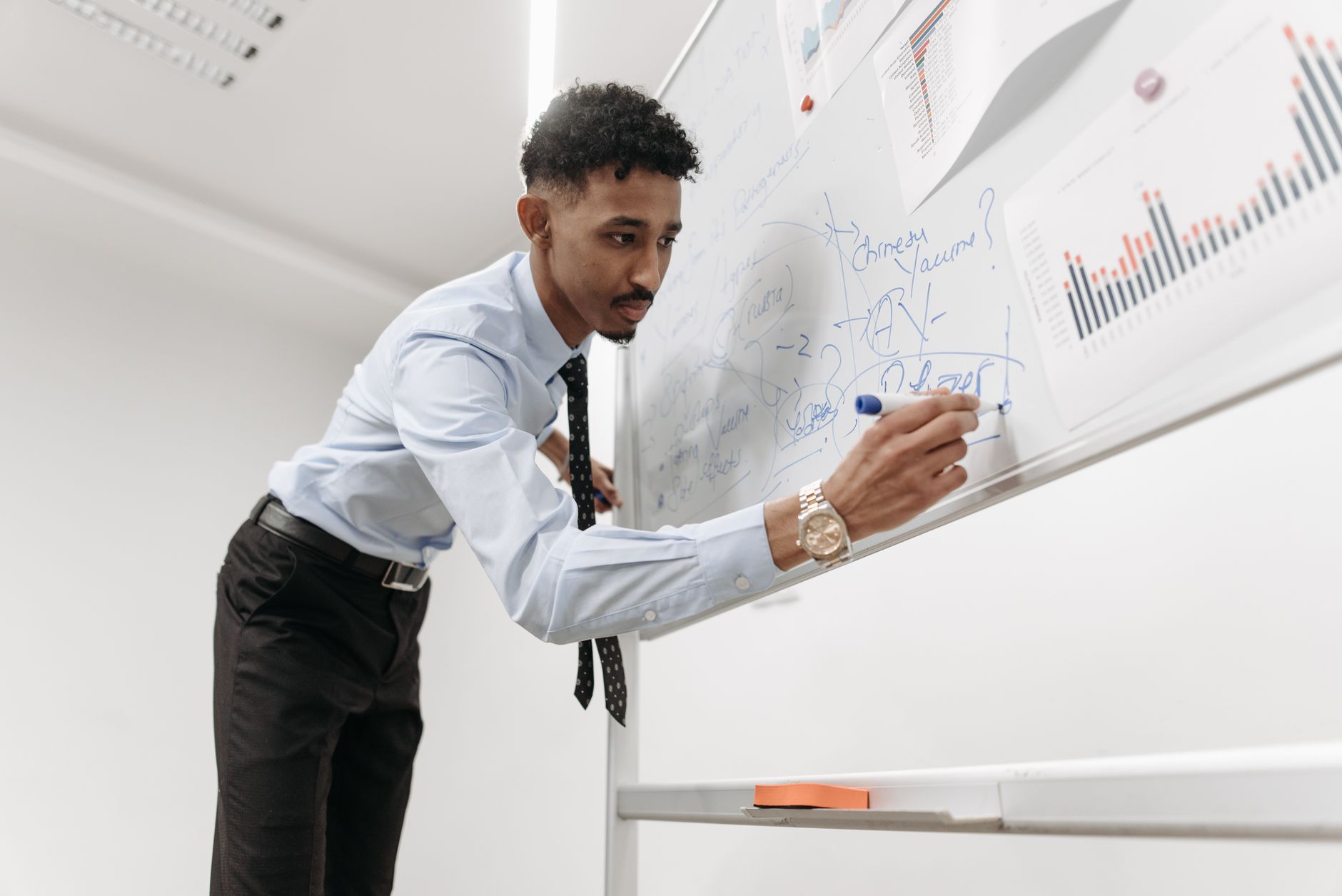 A professional man presenting statistics on a whiteboard in an office setting.