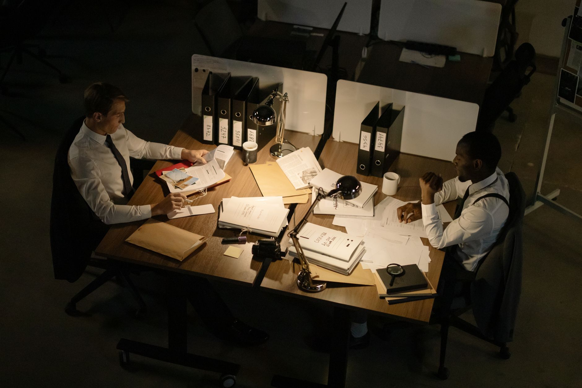 Two businessmen collaborating over documents in a dimly lit office setting.