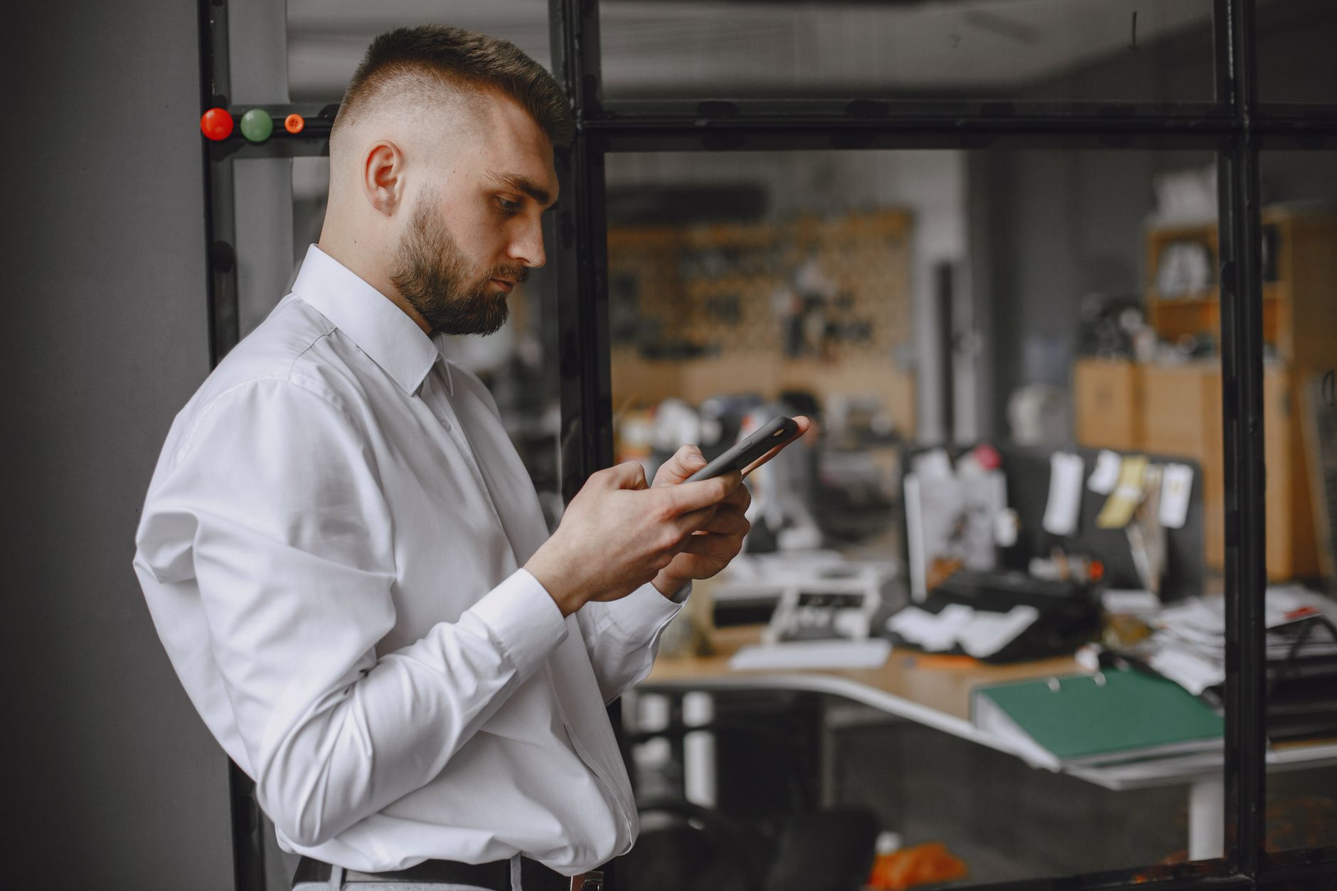 Businessman in white shirt using phone in office, showcasing modern technology and workplace focus.