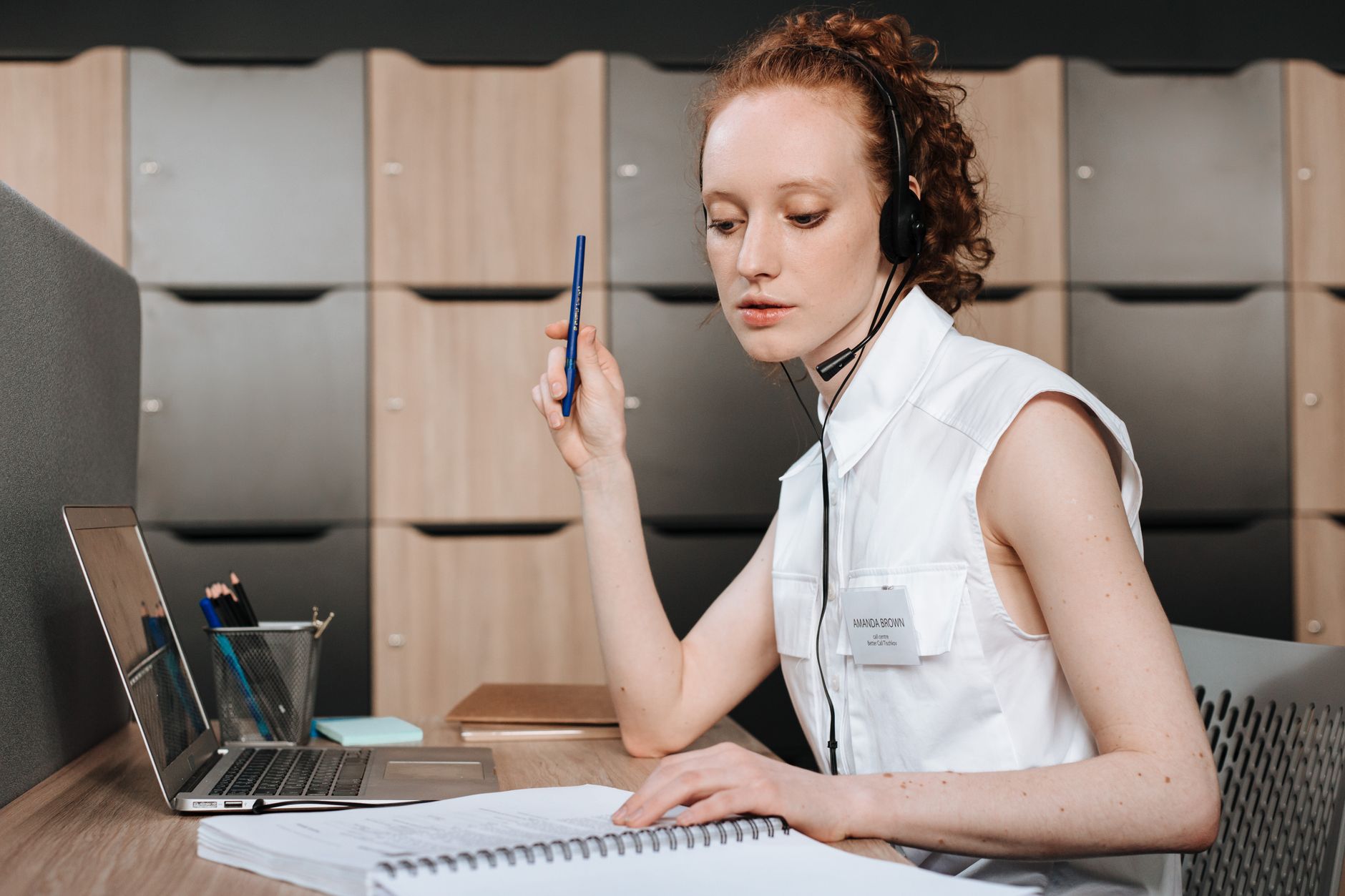 Woman with headset working in customer service at a modern office, using a laptop.