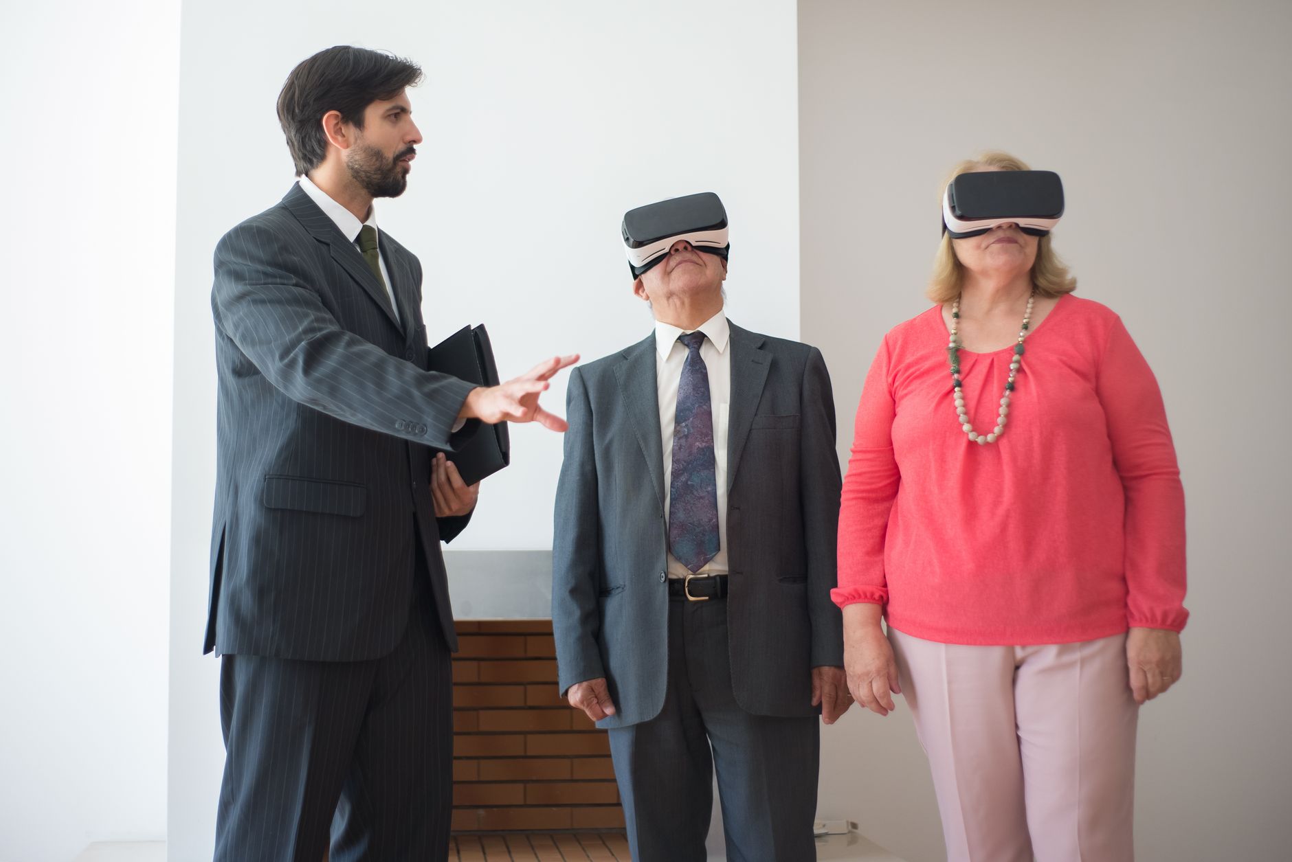 A real estate agent demonstrates a property to a couple using virtual reality technology indoors.