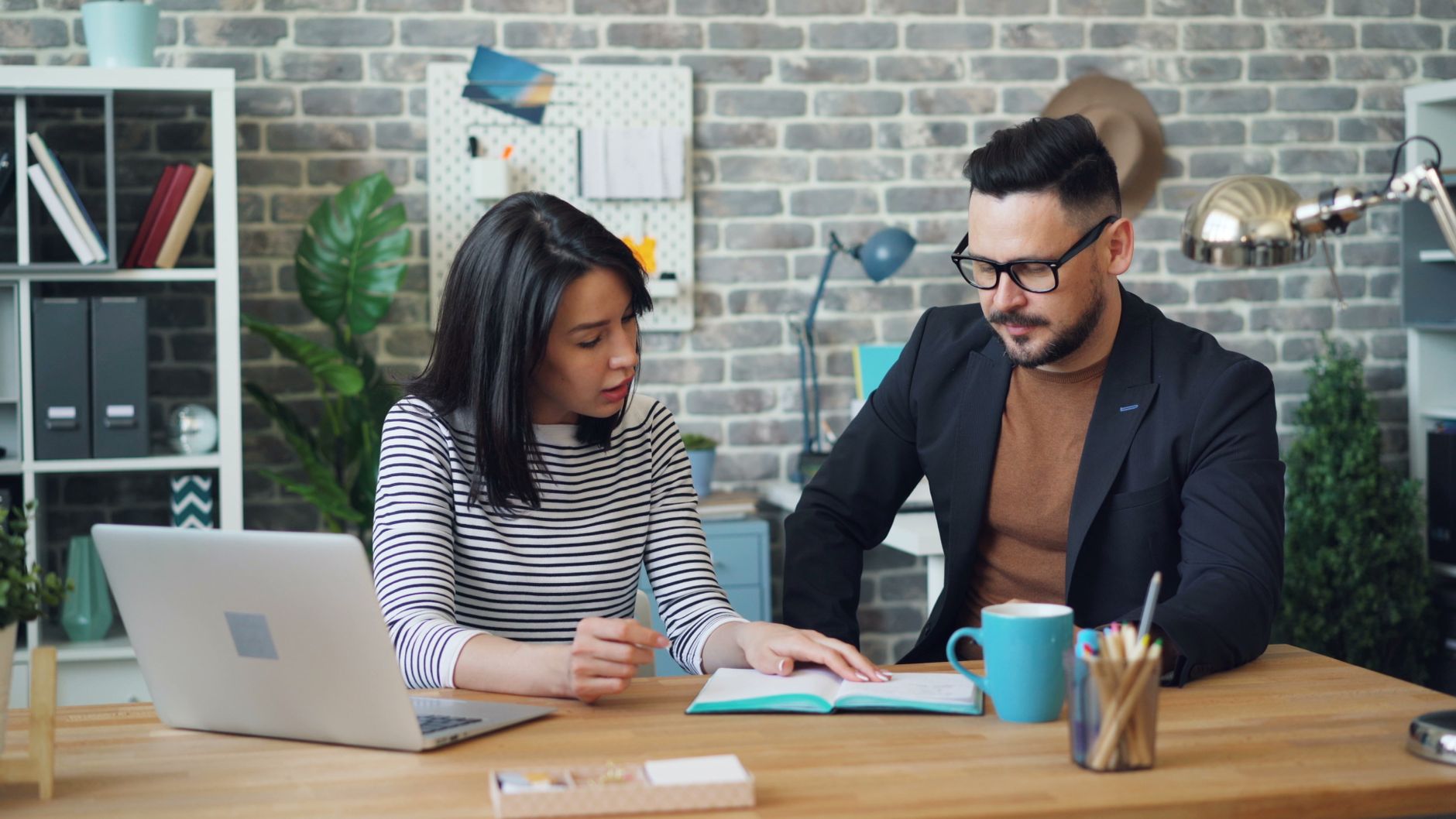 Two professionals discussing strategies at a modern office desk with a laptop.