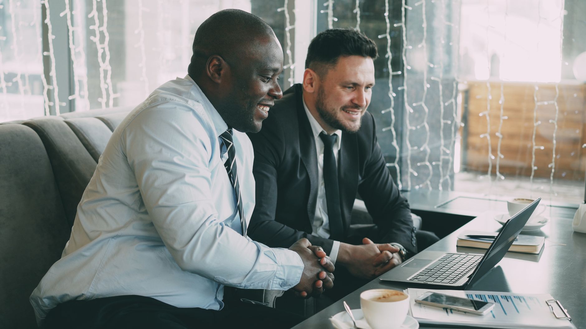 Two businessmen working together on a laptop in a cozy cafe setting.
