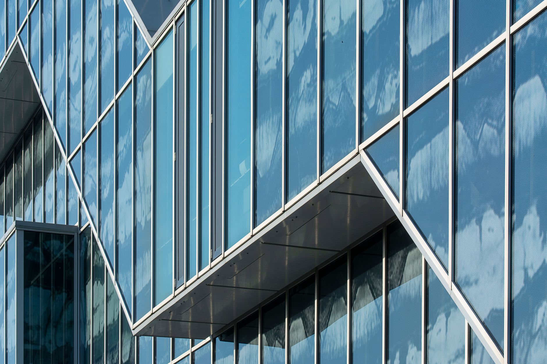 Close-up of modern glass building facade with sky reflections creating a geometric design.