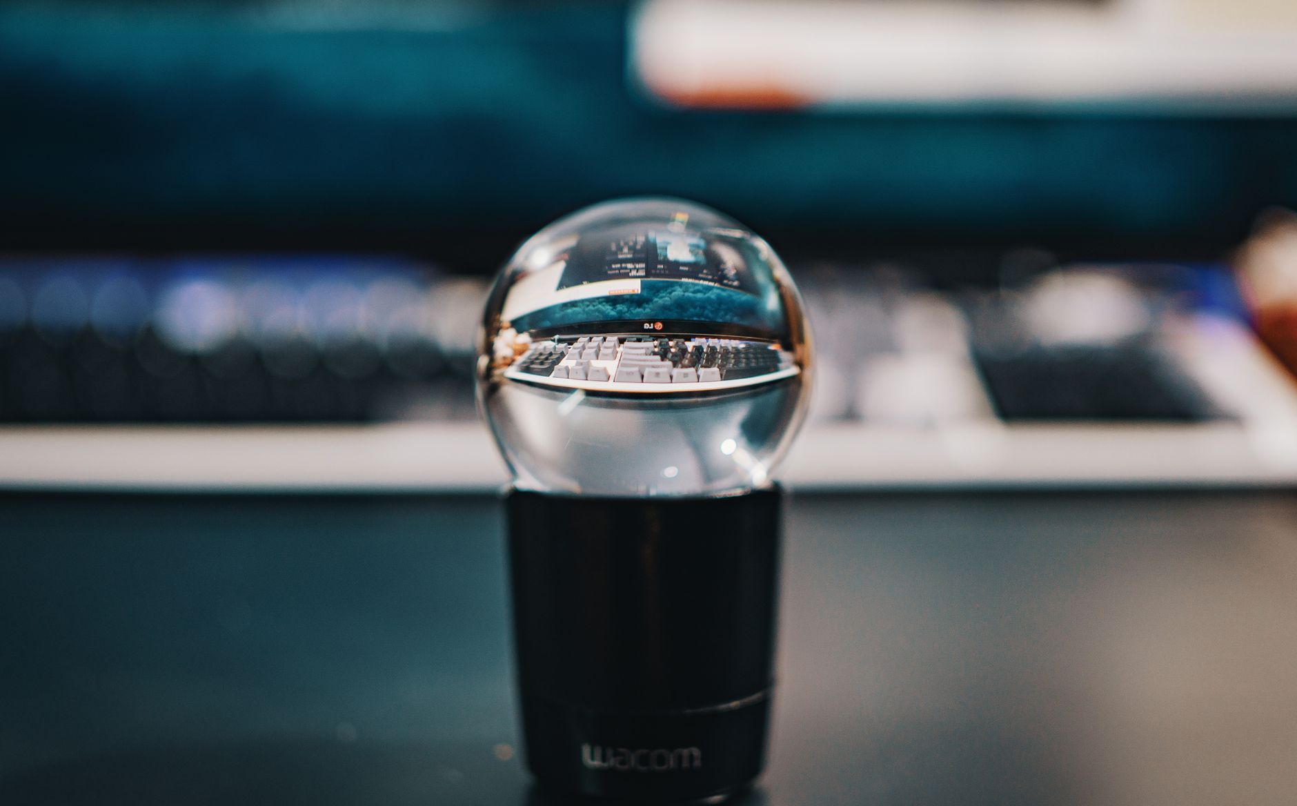A crystal ball capturing a unique reflection of a modern computer keyboard and monitor setup.