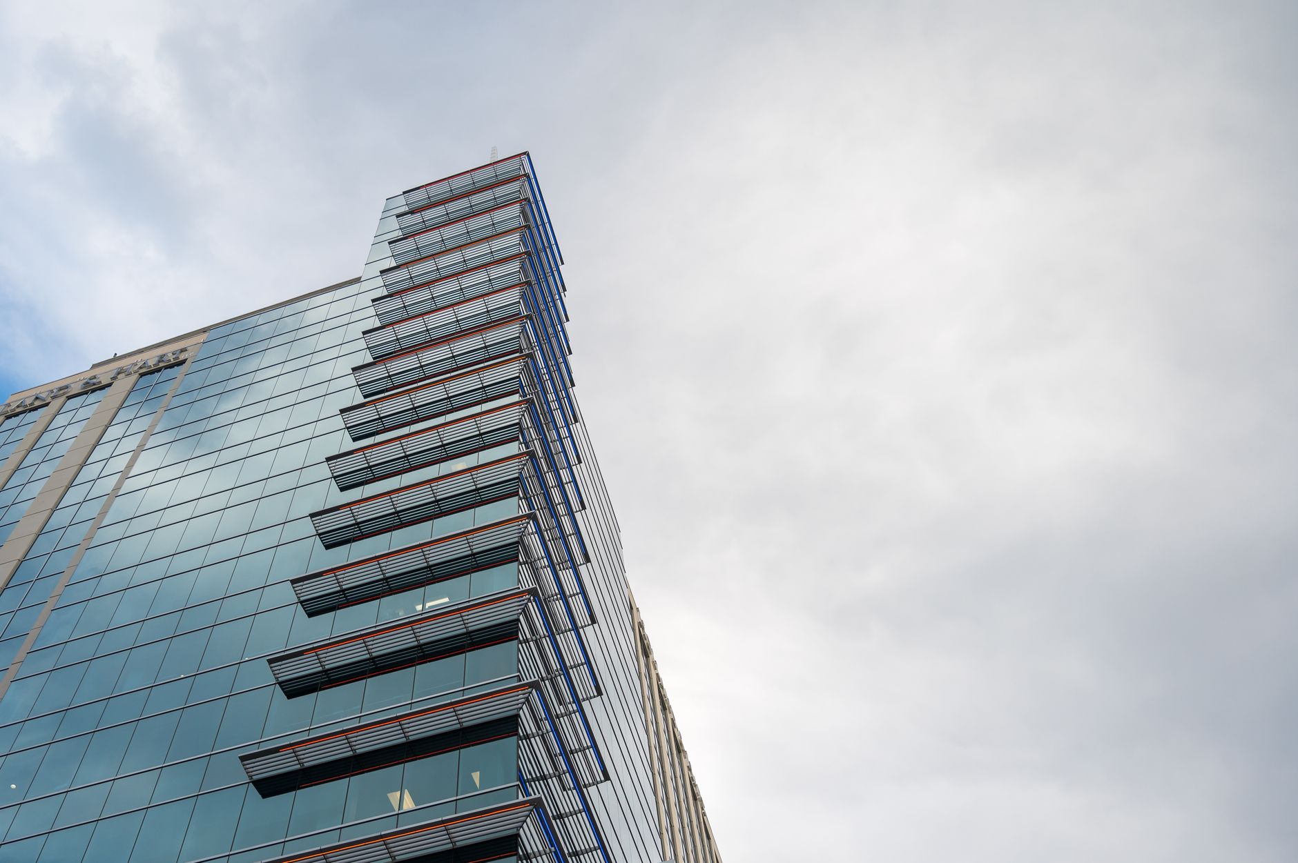 A low angle view of a modern glass skyscraper with a cloudy sky backdrop, highlighting architectural design.