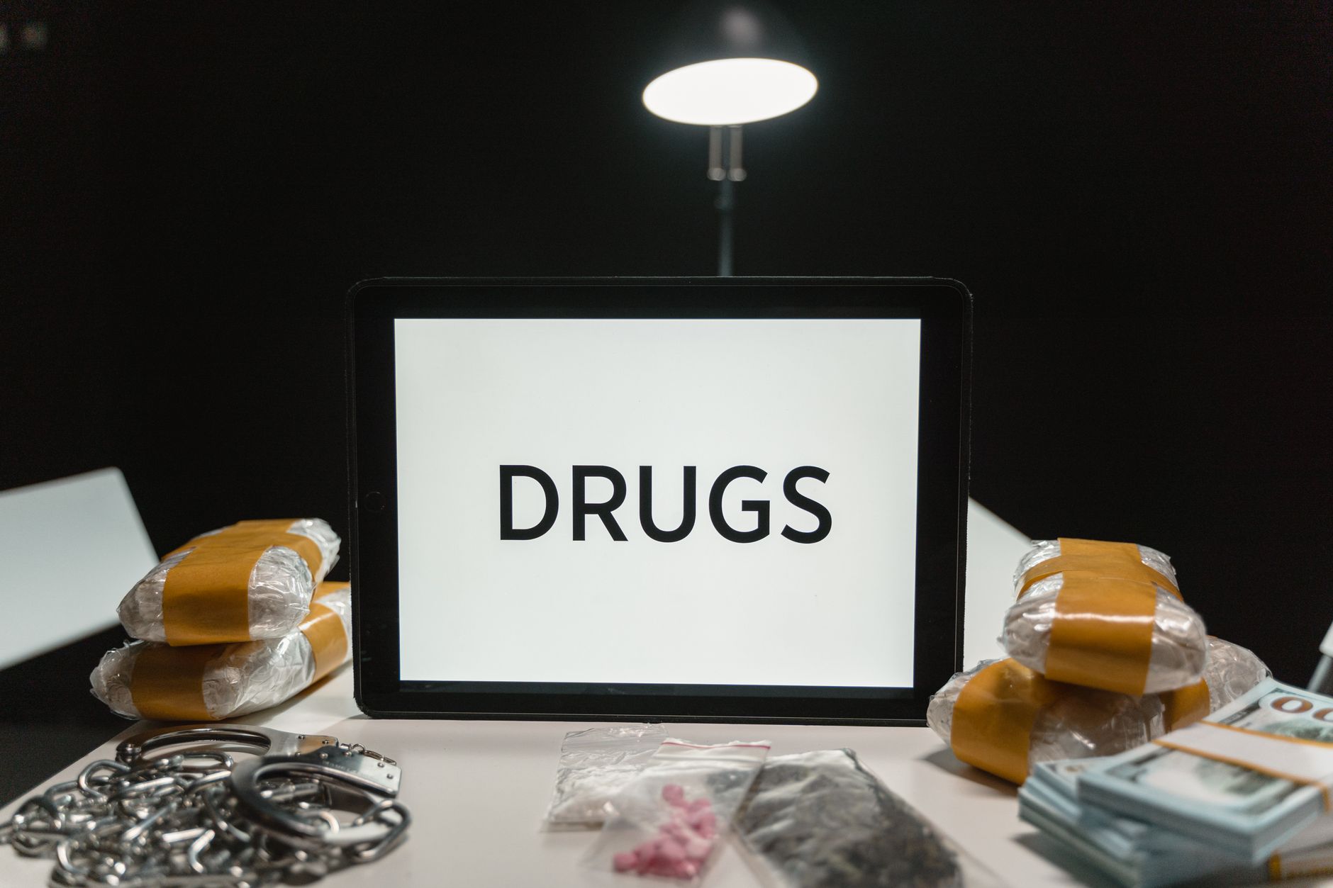 Conceptual image of drugs, money, and handcuffs on a table under harsh light, depicting crime themes.