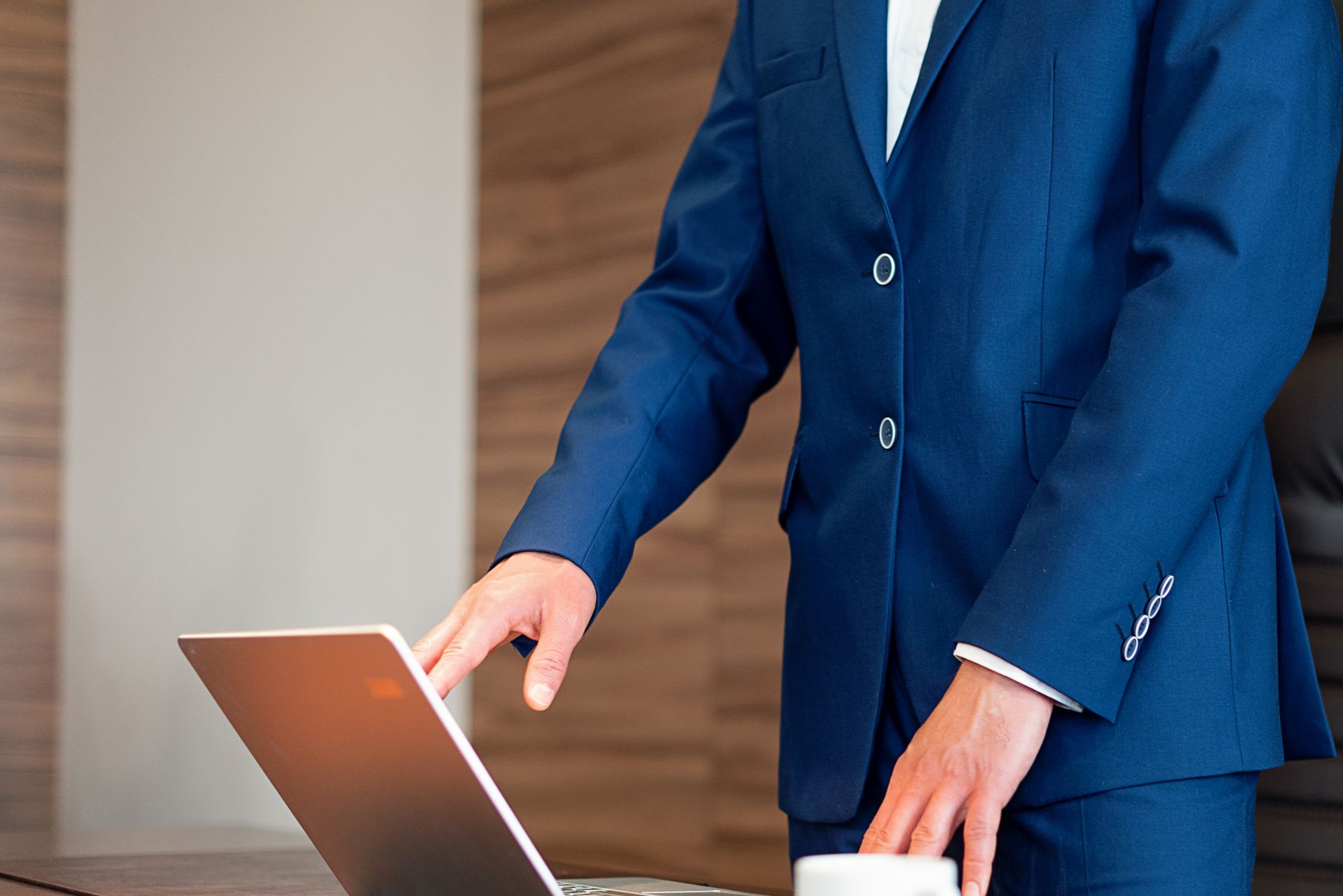 Business professional in a suit using a laptop on a desk in an office setting.
