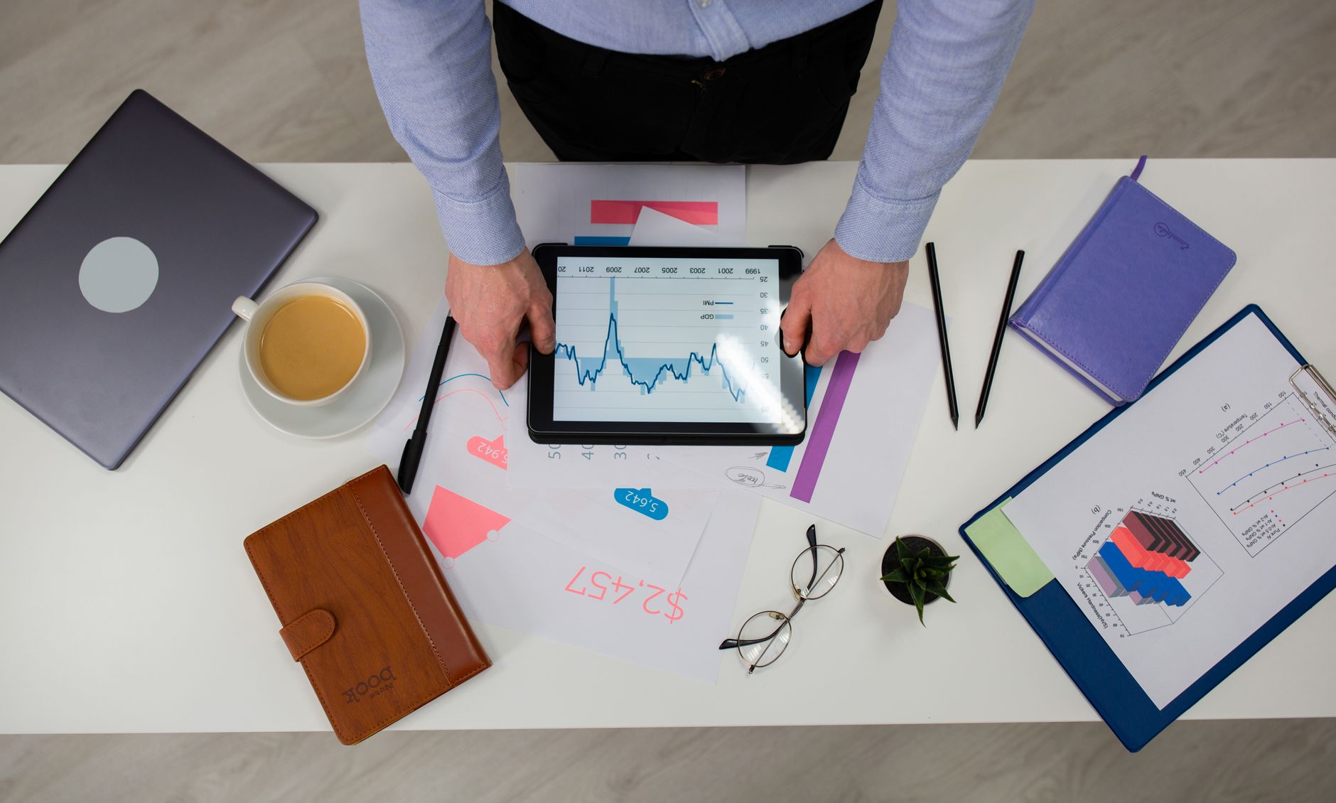 Overhead view of businessman using tablet to review data charts at a modern office desk.