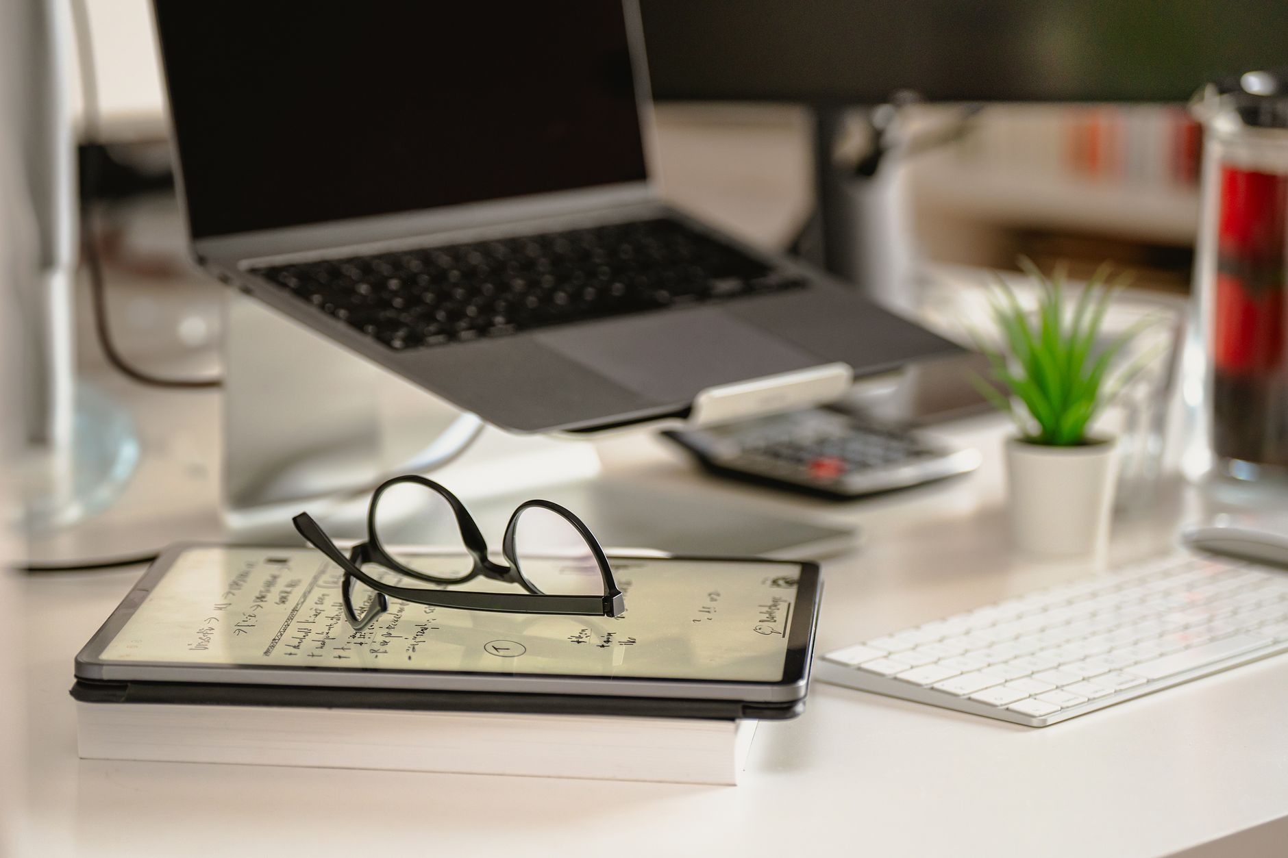 Close-up of a stylish desk with a laptop, tablet, and eyeglasses.